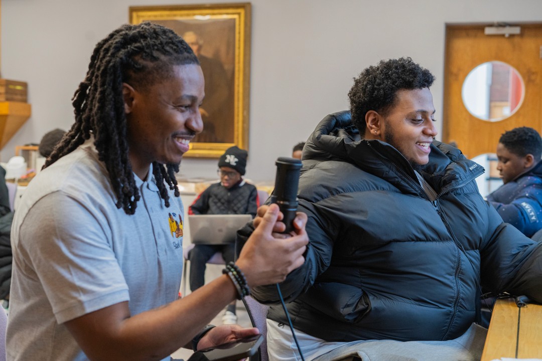 A man passes another man a microphone at an event in London