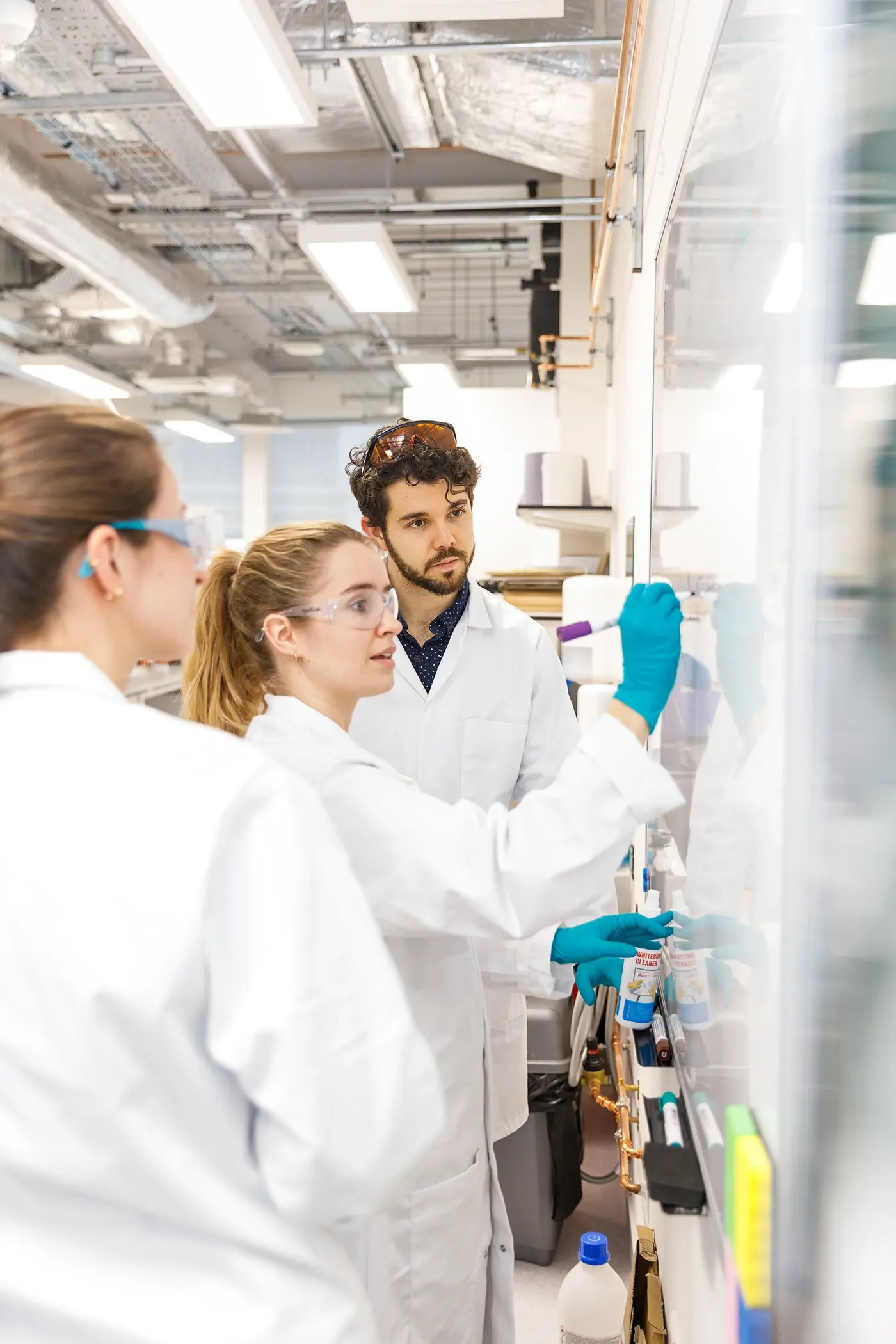 3 people in a lab with one writing on a whiteboard