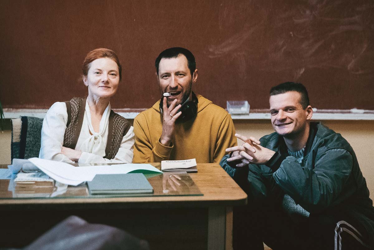 Behind-the-scenes: teacher, Džiugas Grinys (as Rimants), and director Ignas Miškinis on set in classroom during filming of Southern Chronicles, a Lithuanian 90s comedy-drama.