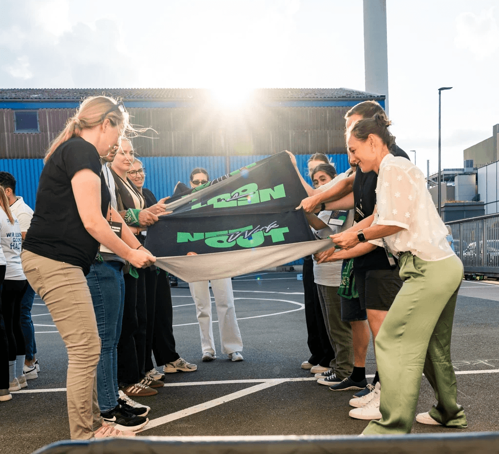 Junge Menschen halten gemeinsam ein Tuch in die Luft, es sieht nach einem Workshop-Spiel aus