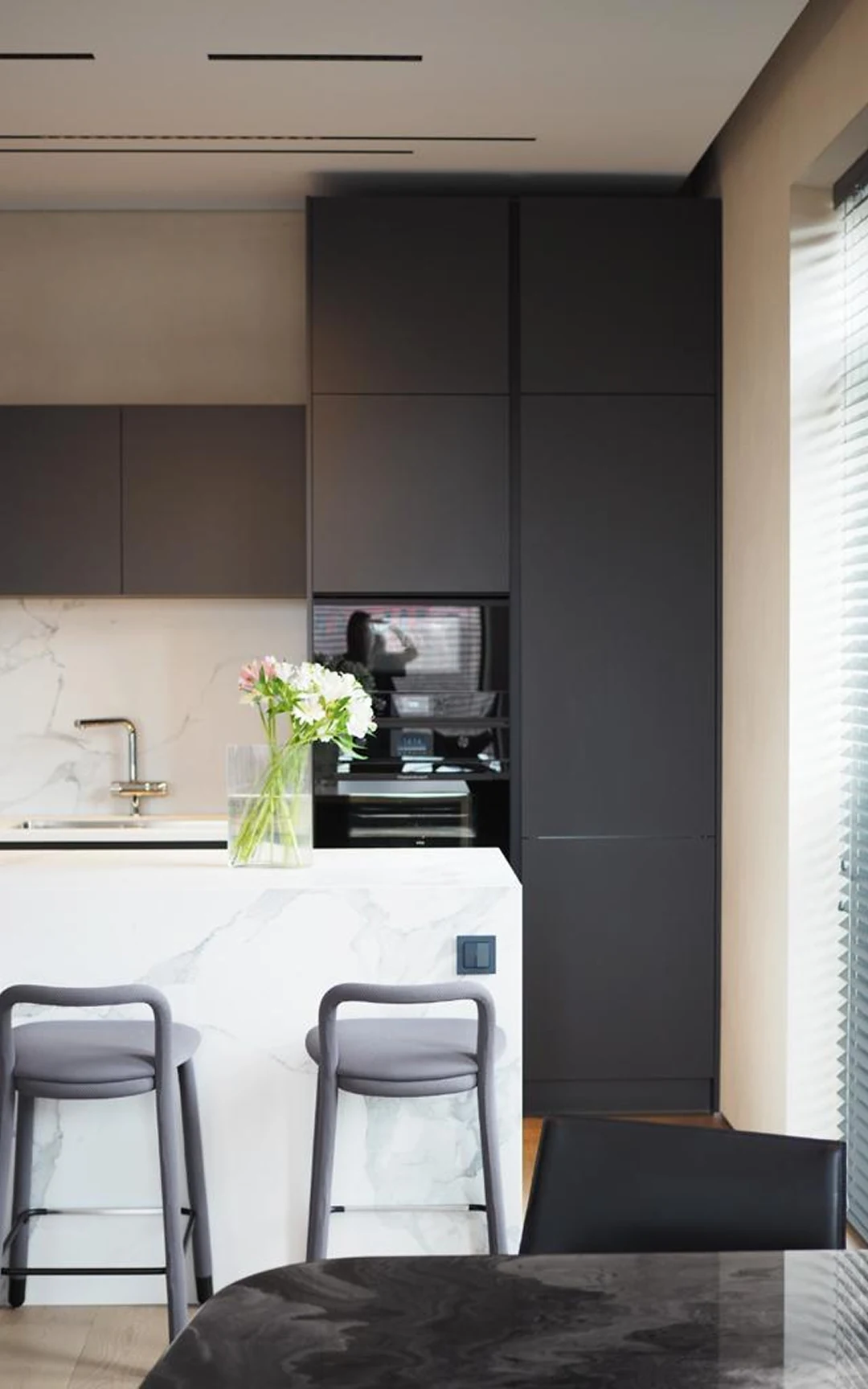 Cuisine contemporaine sur mesure : colonnes gris clair, ilot anthracite, niche appareils avec LED, vitrine à verres éclairée.