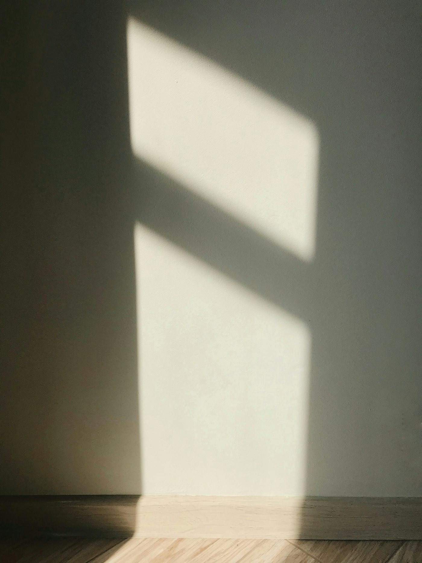 A square of sunlight on a pale wall above a wooden floor