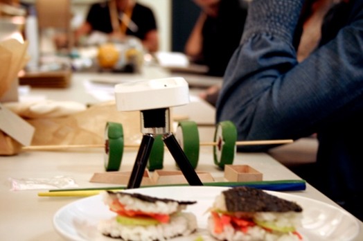A photo of some sandwich food samples and some green sushi rolls on a stick.