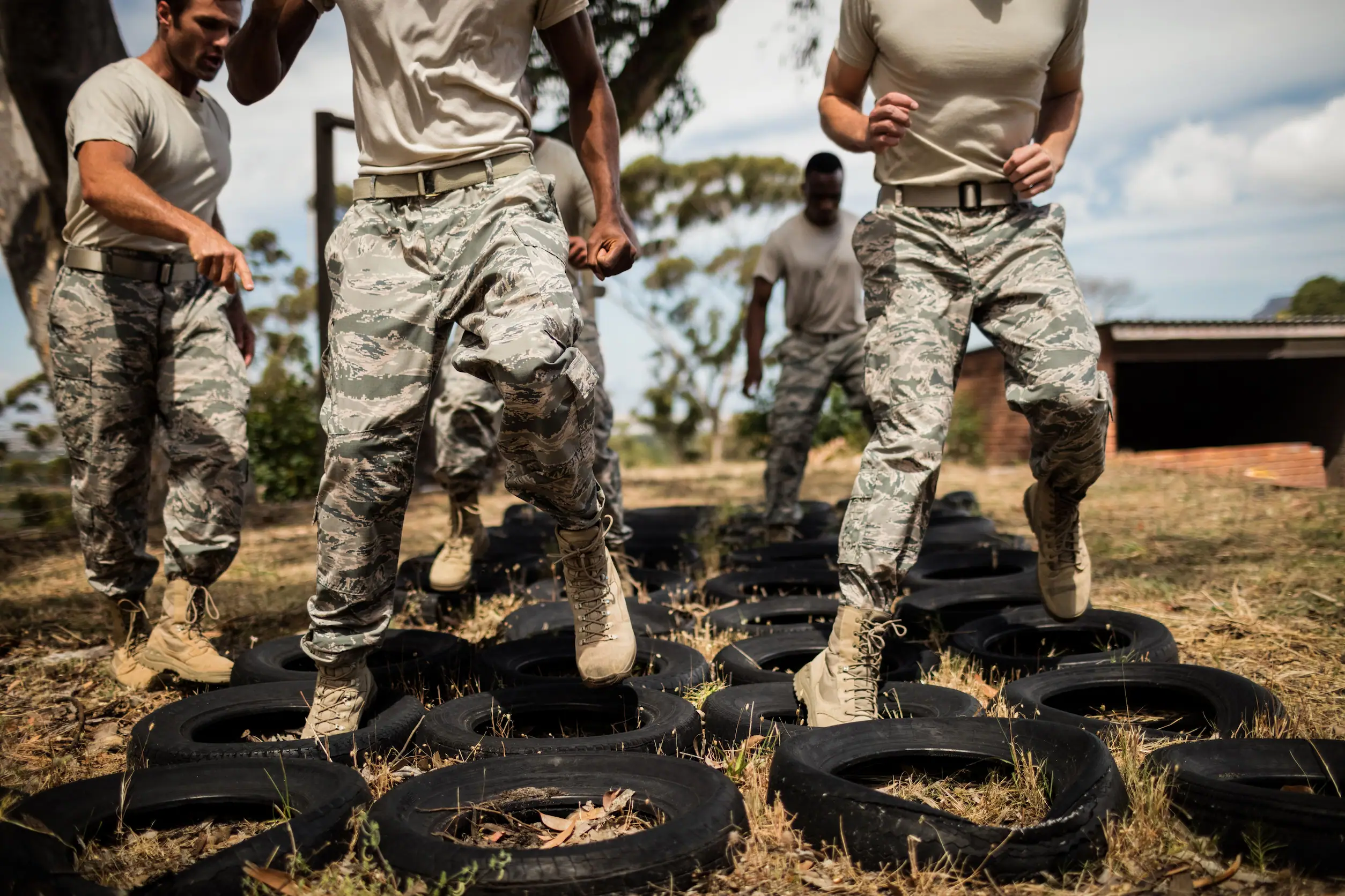 Military personnel in camouflage uniforms running through a tire obstacle course during outdoor training.