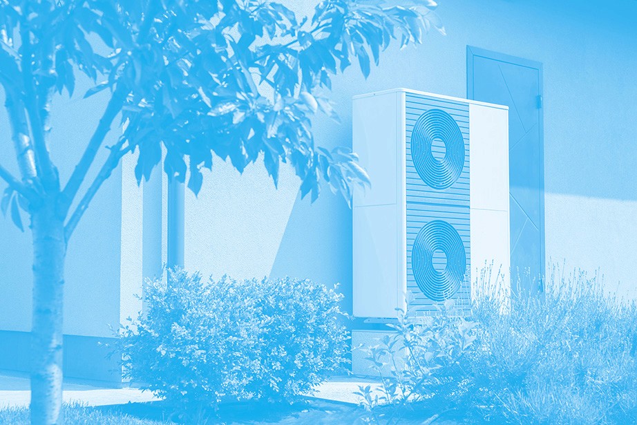 A blue-toned image of an outdoor air conditioning unit placed against a house wall, with surrounding greenery and a tree.