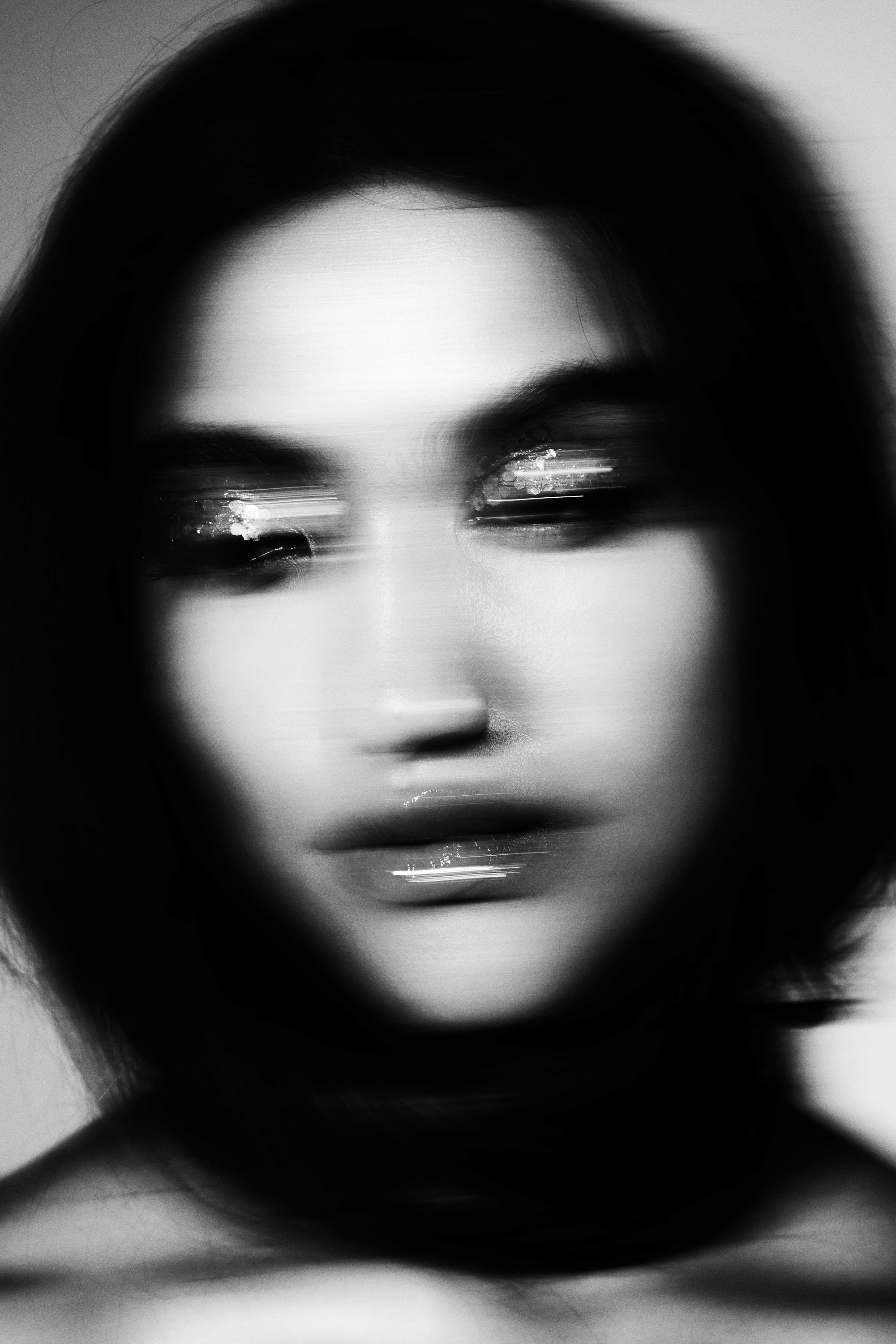 A dramatic black and white beauty photo of a model's face with glittery eyeshadow streaks due to motion blur.