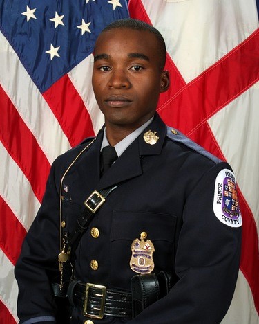 Adrian Morris wearing ploce uniform and posing in front of an american flag