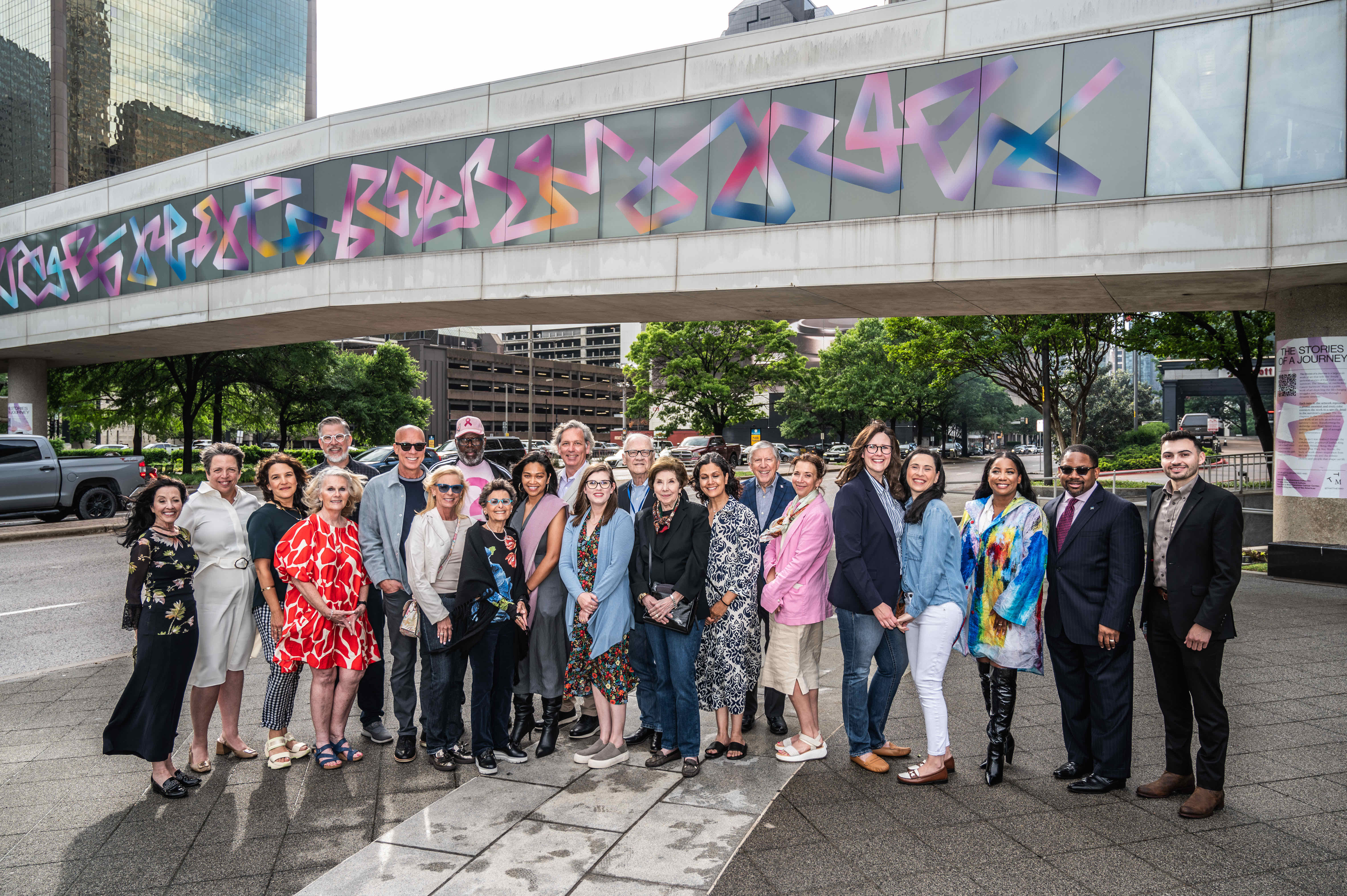 A diverse group of people poses together outdoors in front of a modern building, smiling and dressed in various styles.