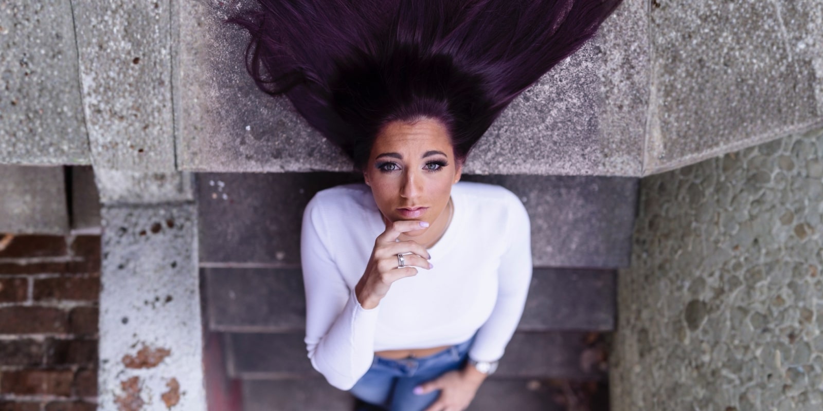 The image shows Diana "Goodvibes" Cosentino looking up while seated on stairs, with long purple hair flowing around her.