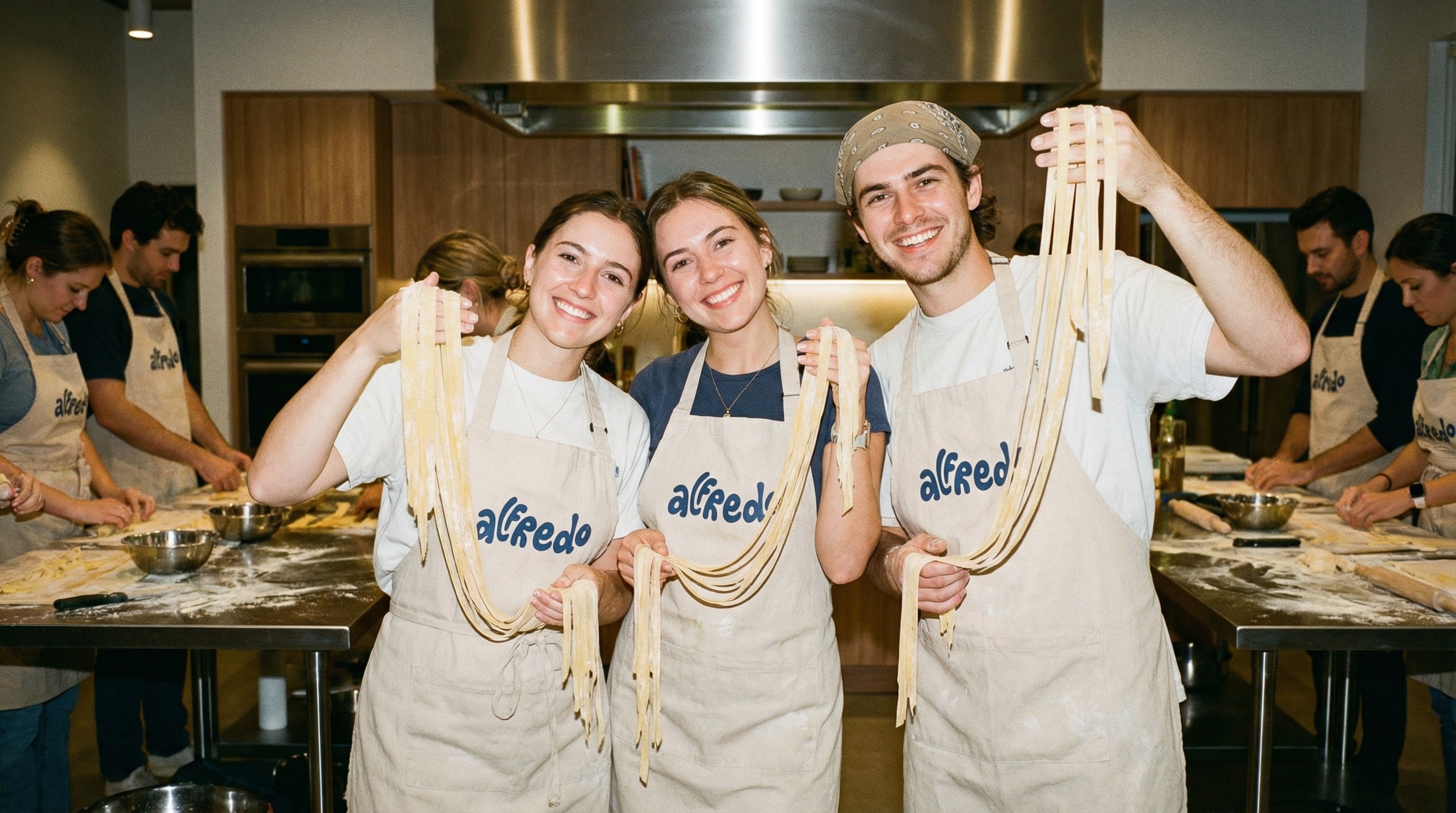 Participants during Alfredo fresh pasta cooking class holding handmade tagliatelle in a contemporary Italian kitchen