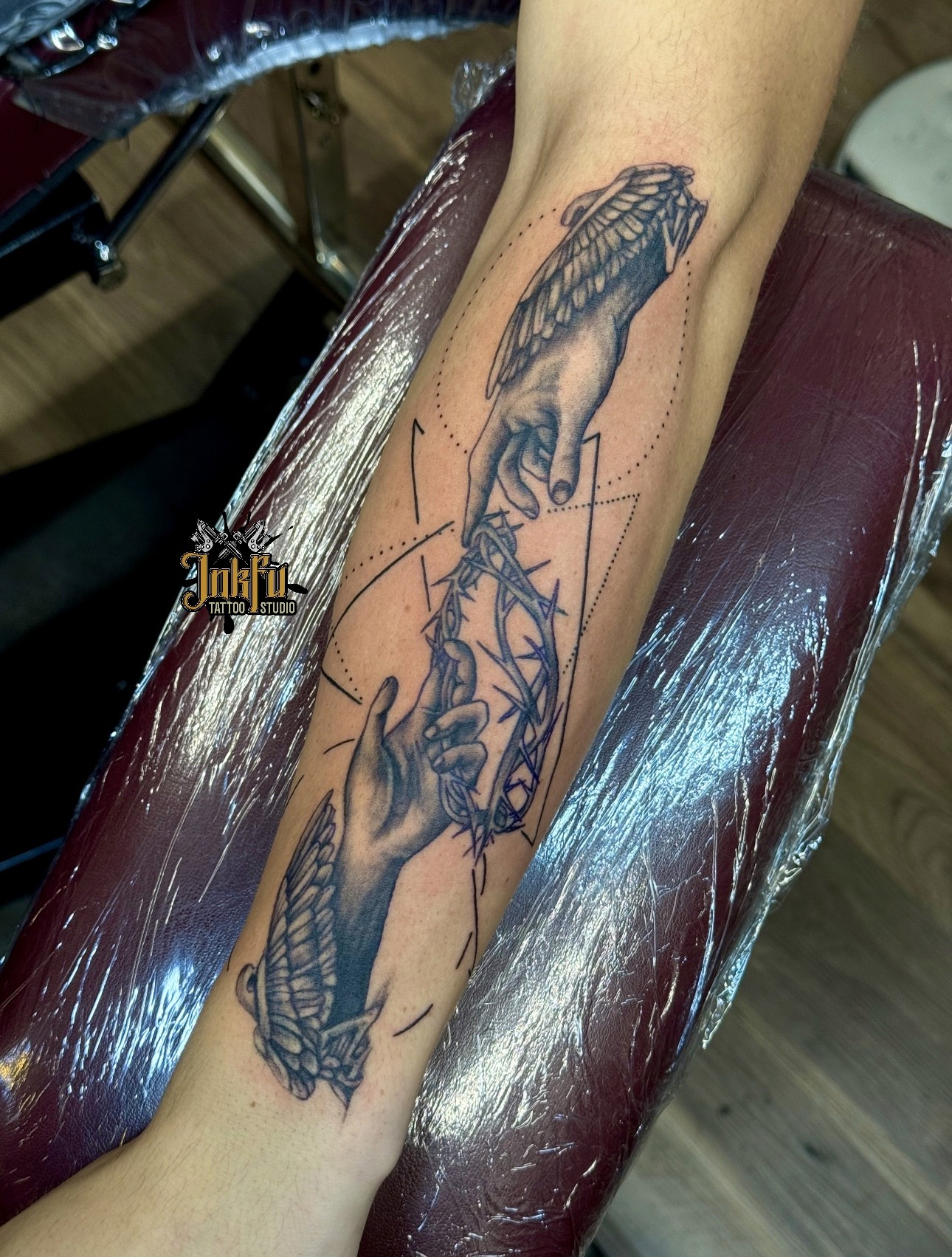 Black and grey tattoo of winged hands holding a crown of thorns on the forearm, by Meer Rich