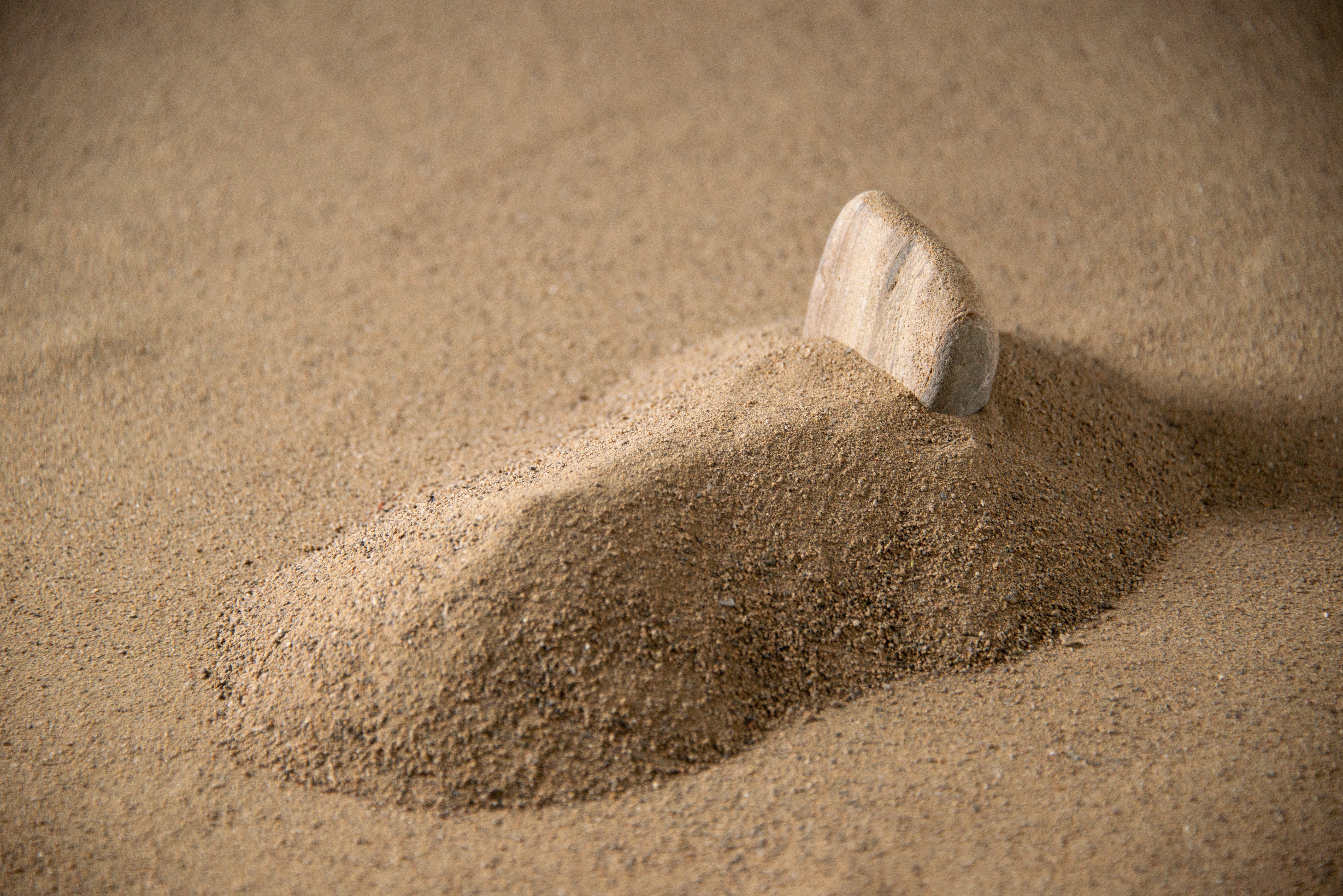 A small mound of sand with a single smooth stone acting as a marker.