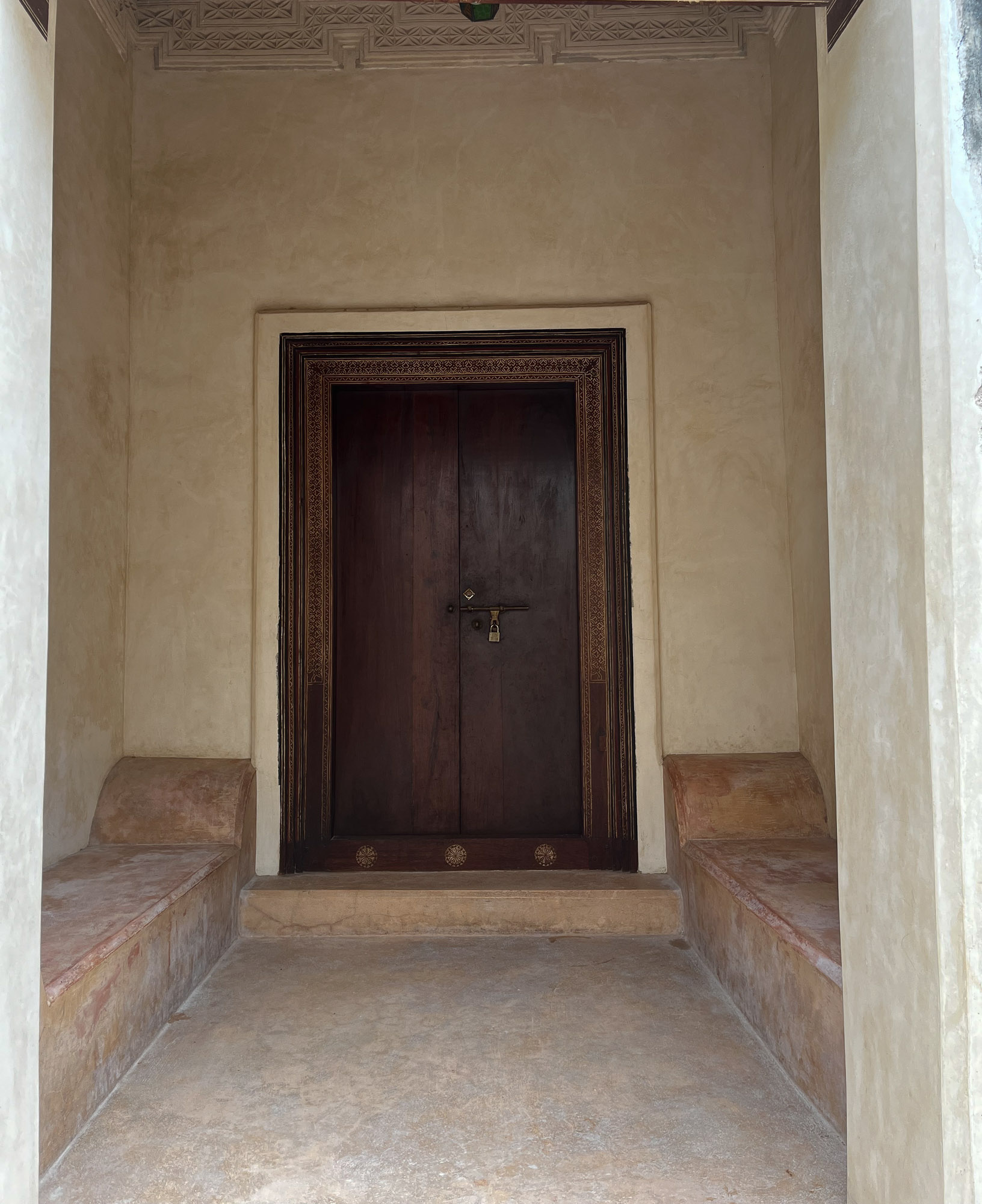 A wooden door in an entrway with stone benches on both sides.