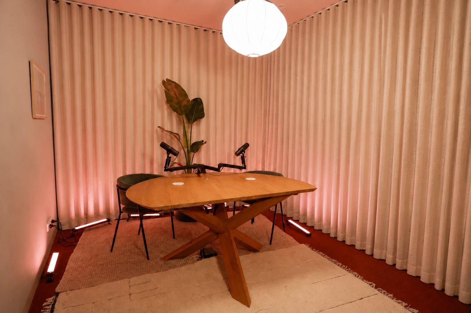 ARC – Collingwood: an oval wooden table with microphones and a plant, framed by pink-toned curtains