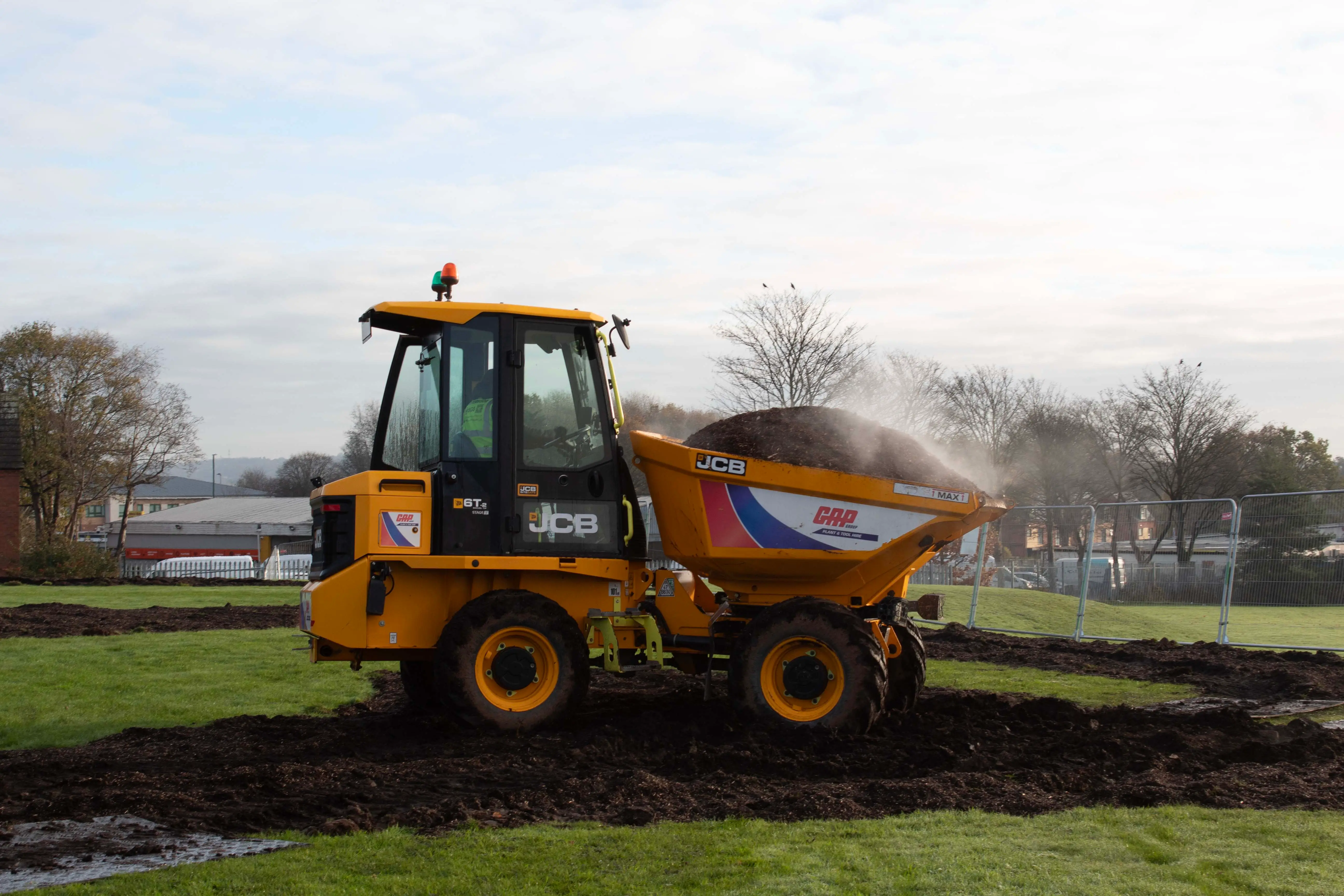 A yellow dumper truck parked on a grassy area, with trees and a cloudy sky in the background.