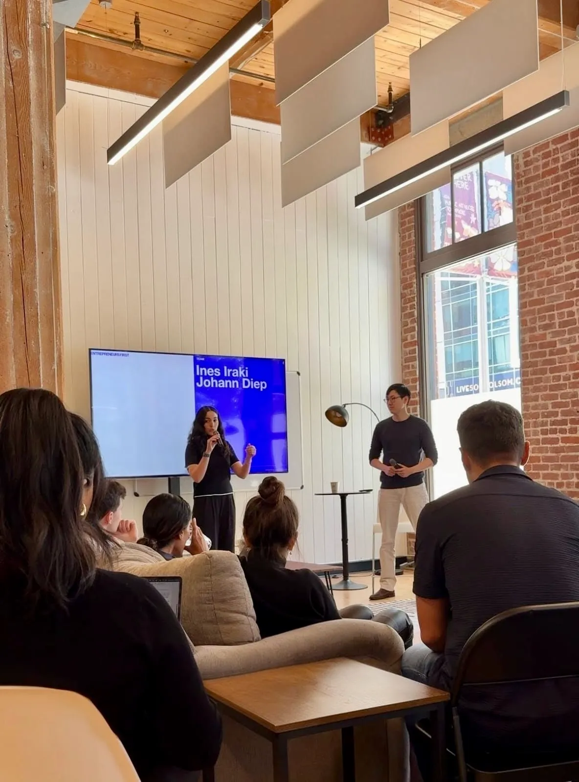 employees of uncovr ai speaking at an event with a tv screen in the background