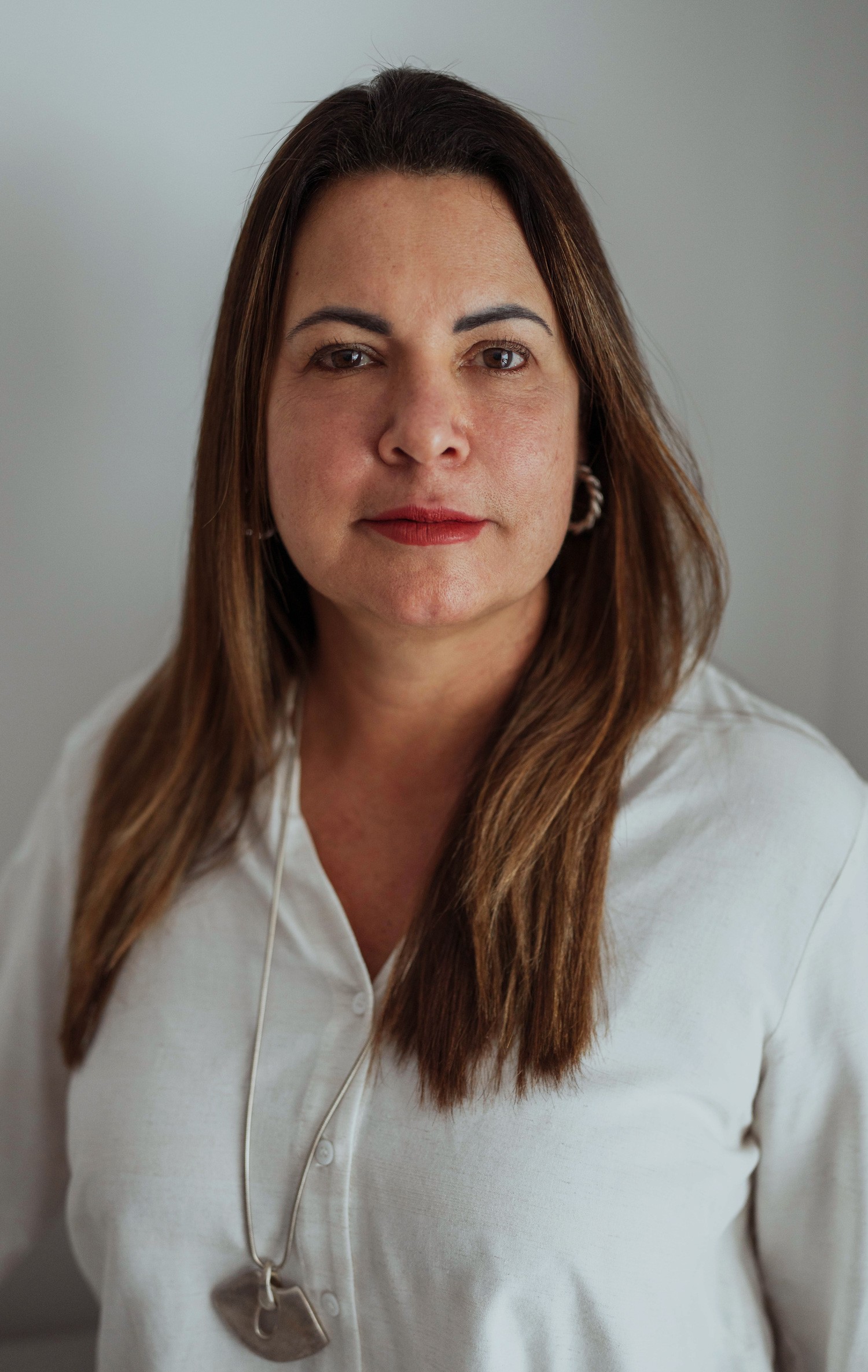 Smiling female therapist with short gray hair, wearing a brown top and a purple shawl, surrounded by a cozy background.
