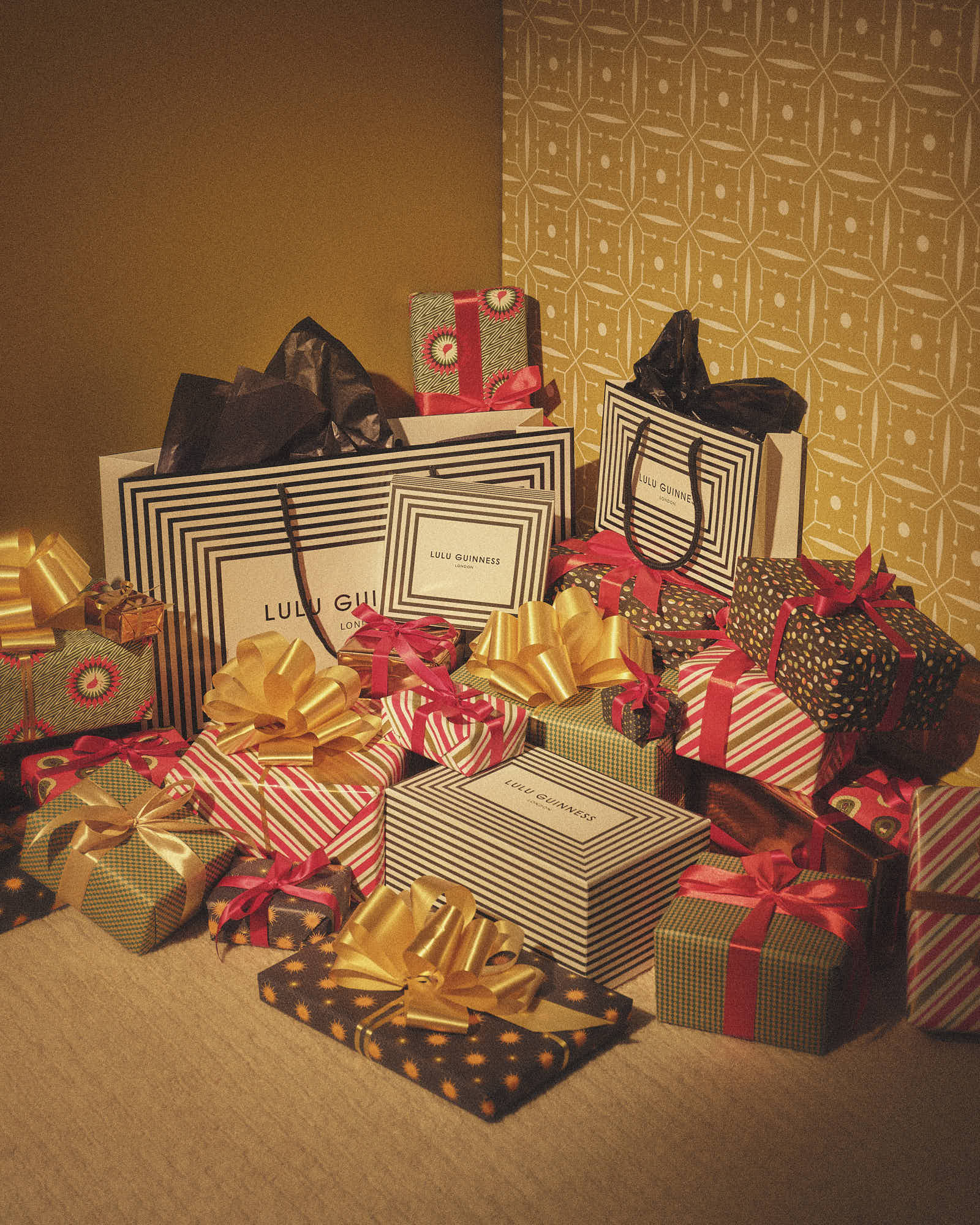 Colorful gift boxes with bows and Lulu Guinness bags on a festive backdrop.