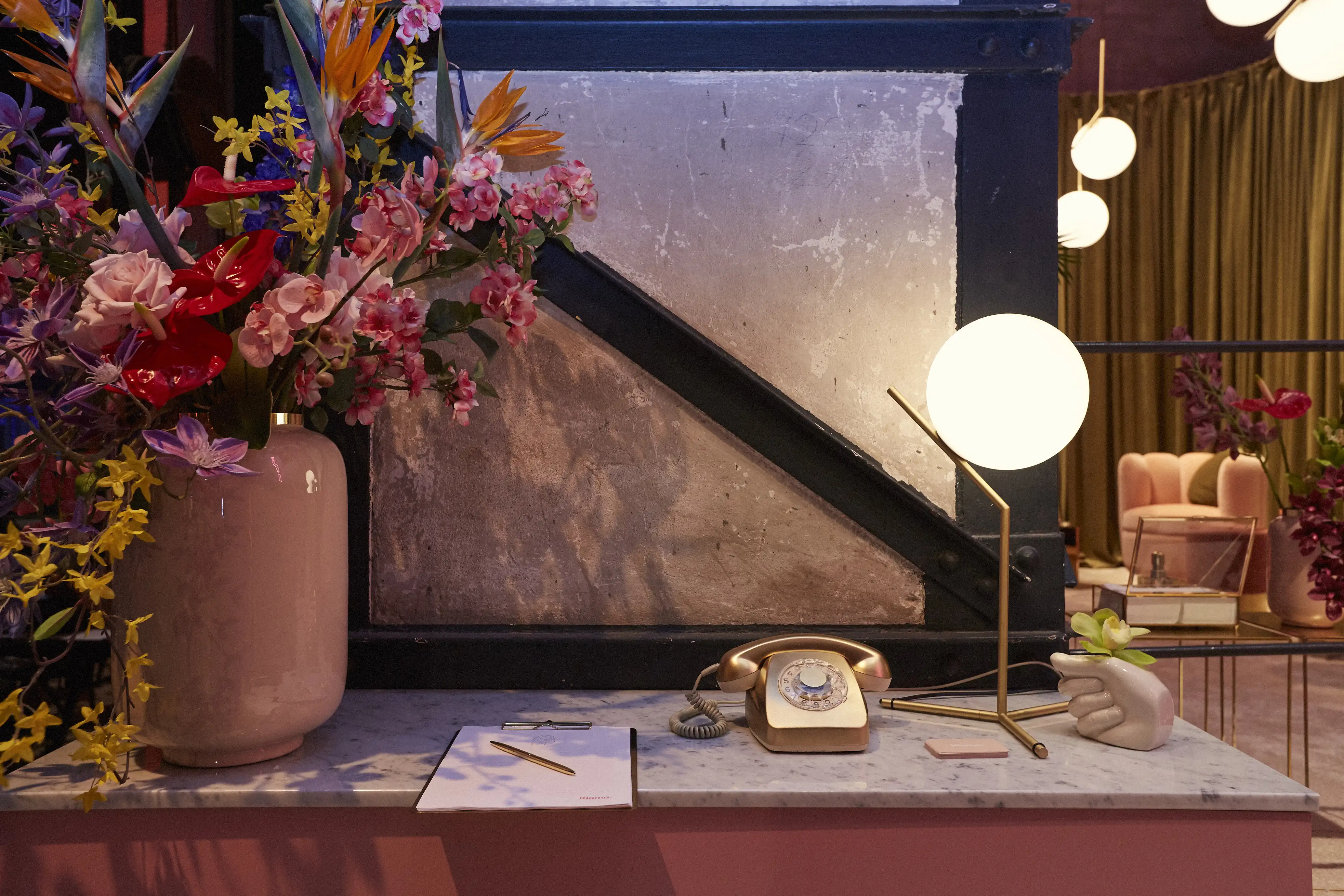 Styling detail at the Klarna pop-up during Berlin Fashion Week: vintage rose-gold telephone, glass globe lamp and lush flower bouquet on a marble counter.