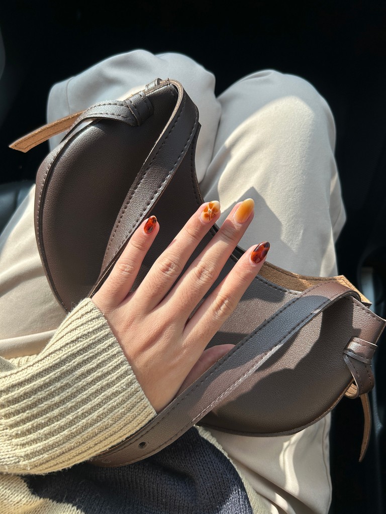 Hand with autumn-colored nails holding a brown purse