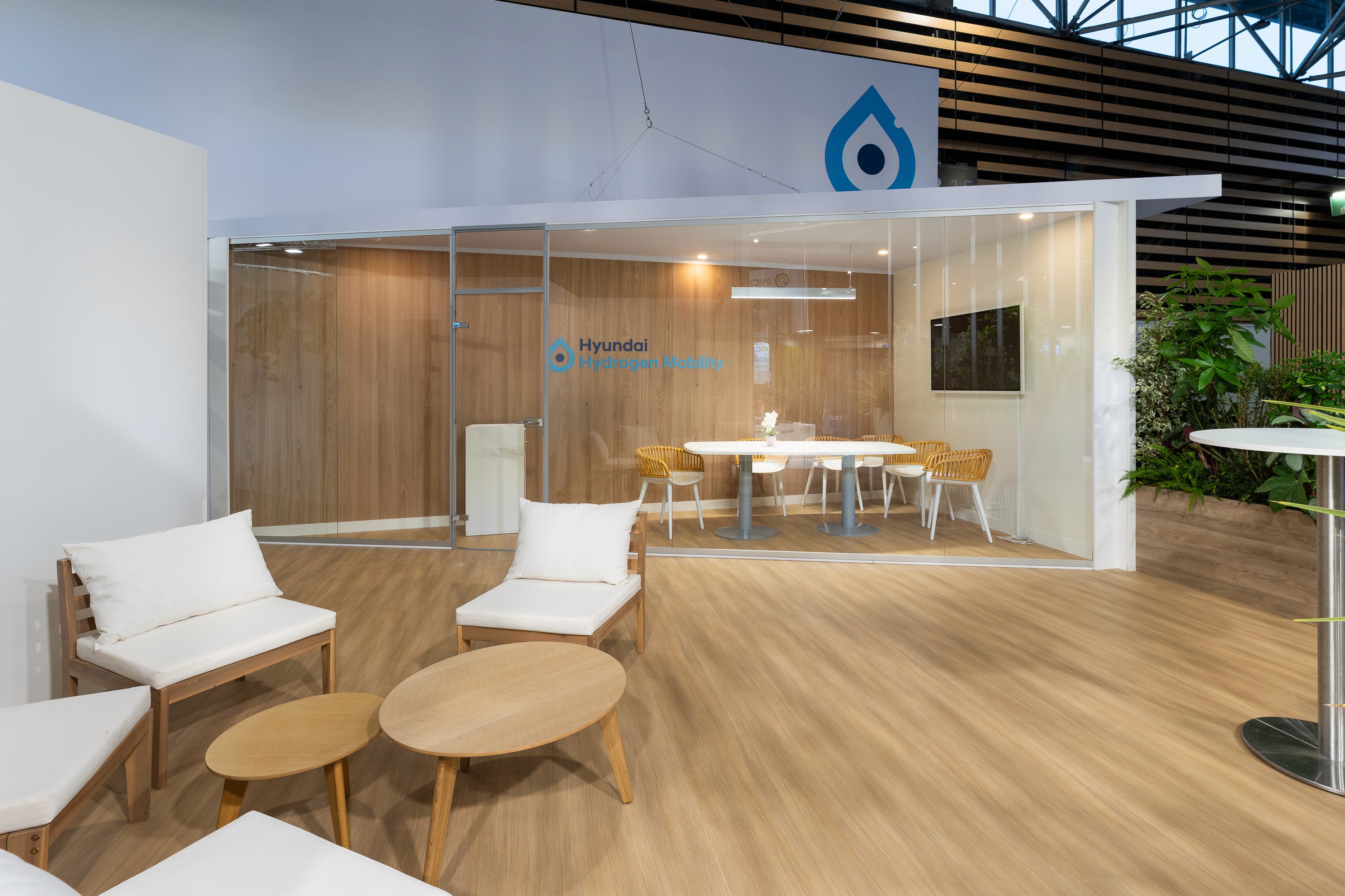 Stand Hyundai Solutrans Lyon 2026 par Expace – espace lounge premium avec mobilier bois organique, sol parquet clair, mur pierre naturelle et ambiance lumineuse tamisée
