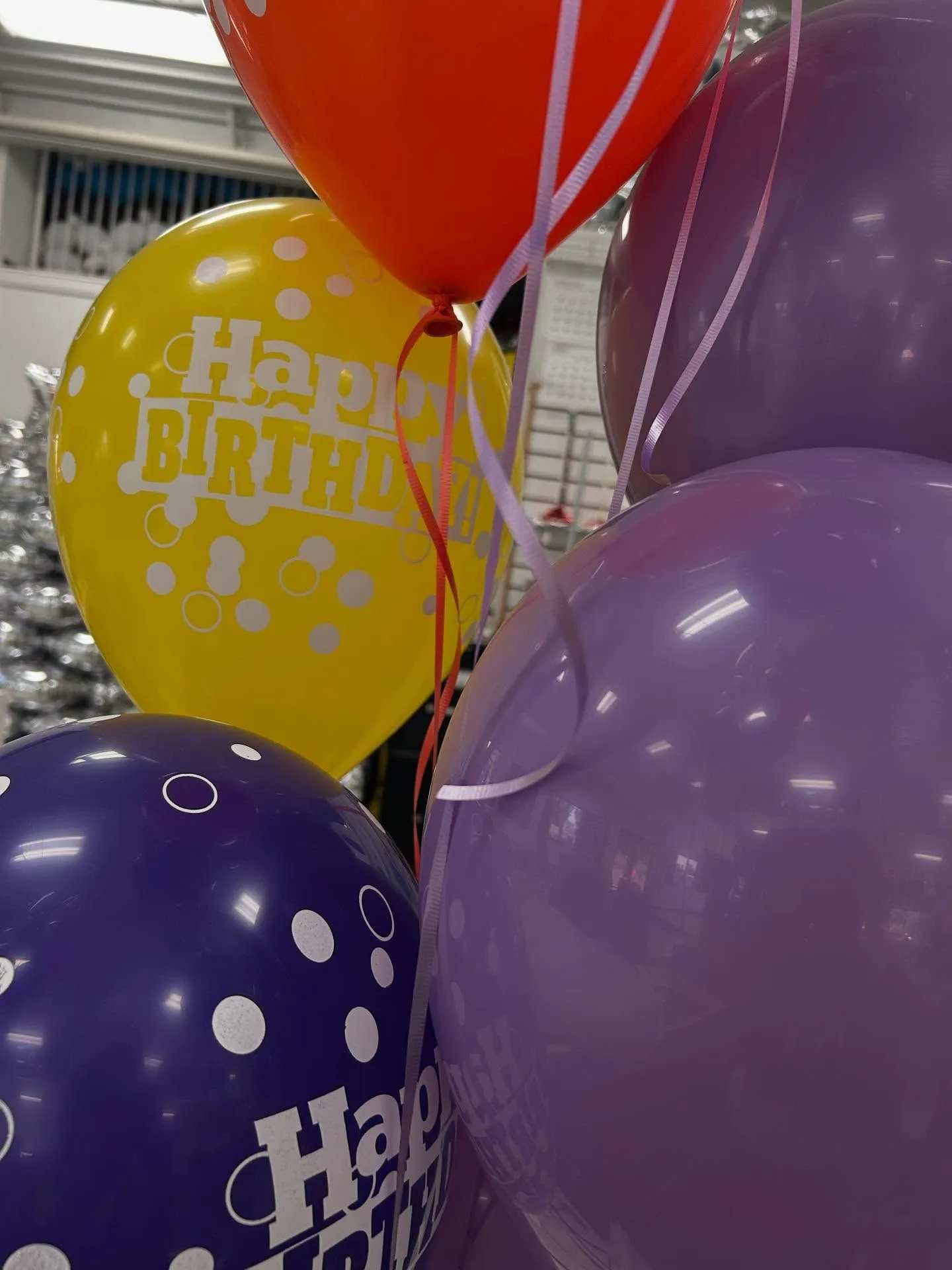 Colorful balloons featuring "Happy Birthday" messages and polka dots are gathered together, including vibrant yellow, purple, and red shades, creating a festive atmosphere.