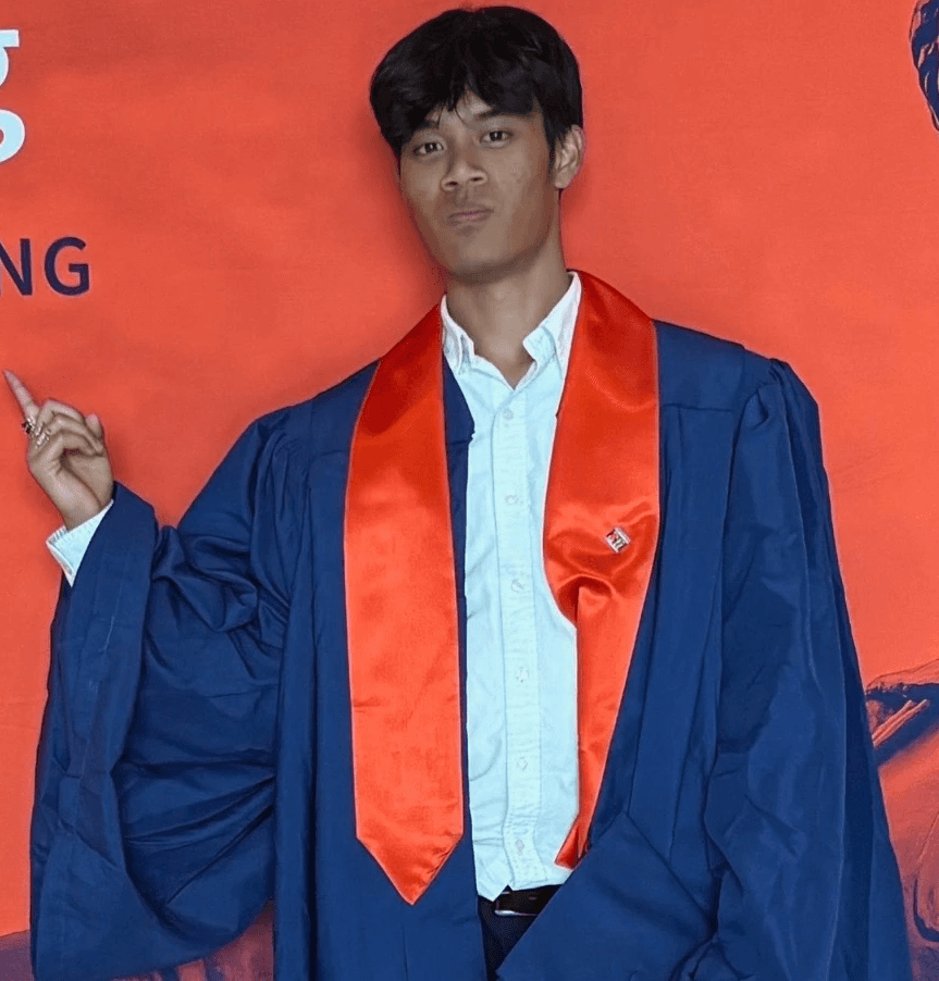 A confident person with short, styled hair and a leather jacket poses against a dark backdrop.