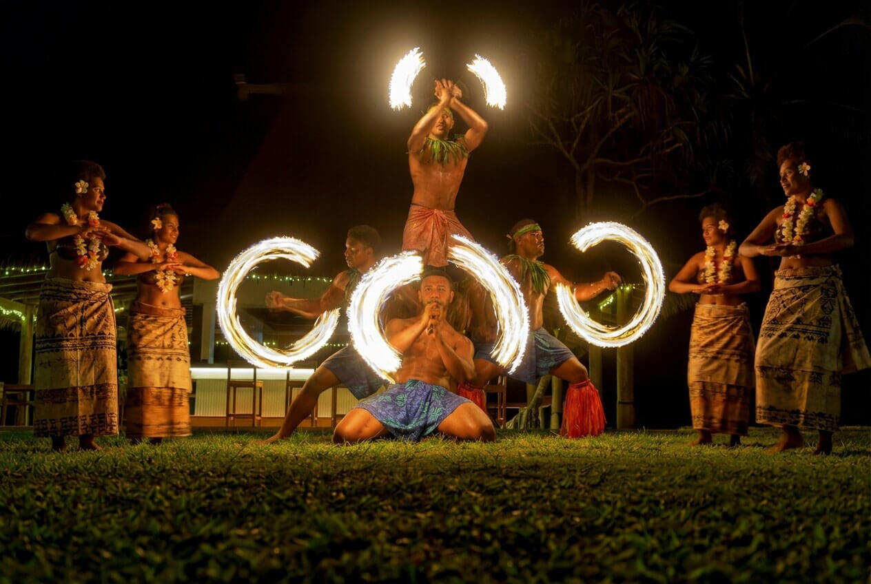 Energetic Fijian fire dancer in traditional attire at Uprising Beach Resort, spinning brilliant arcs of flame at night.