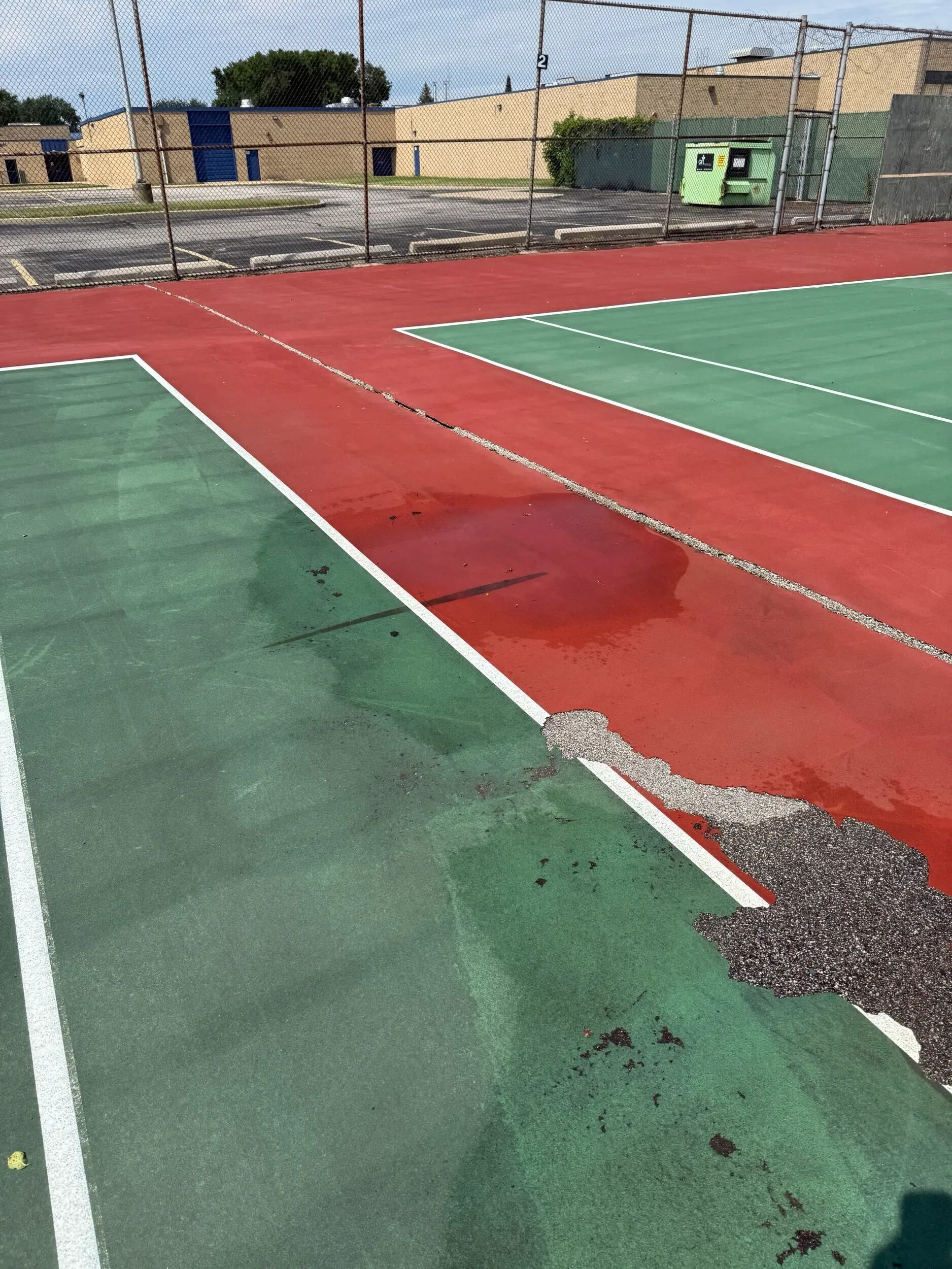 Damaged tennis court surface with extensive cracking before pickleball conversion in Clinton Township