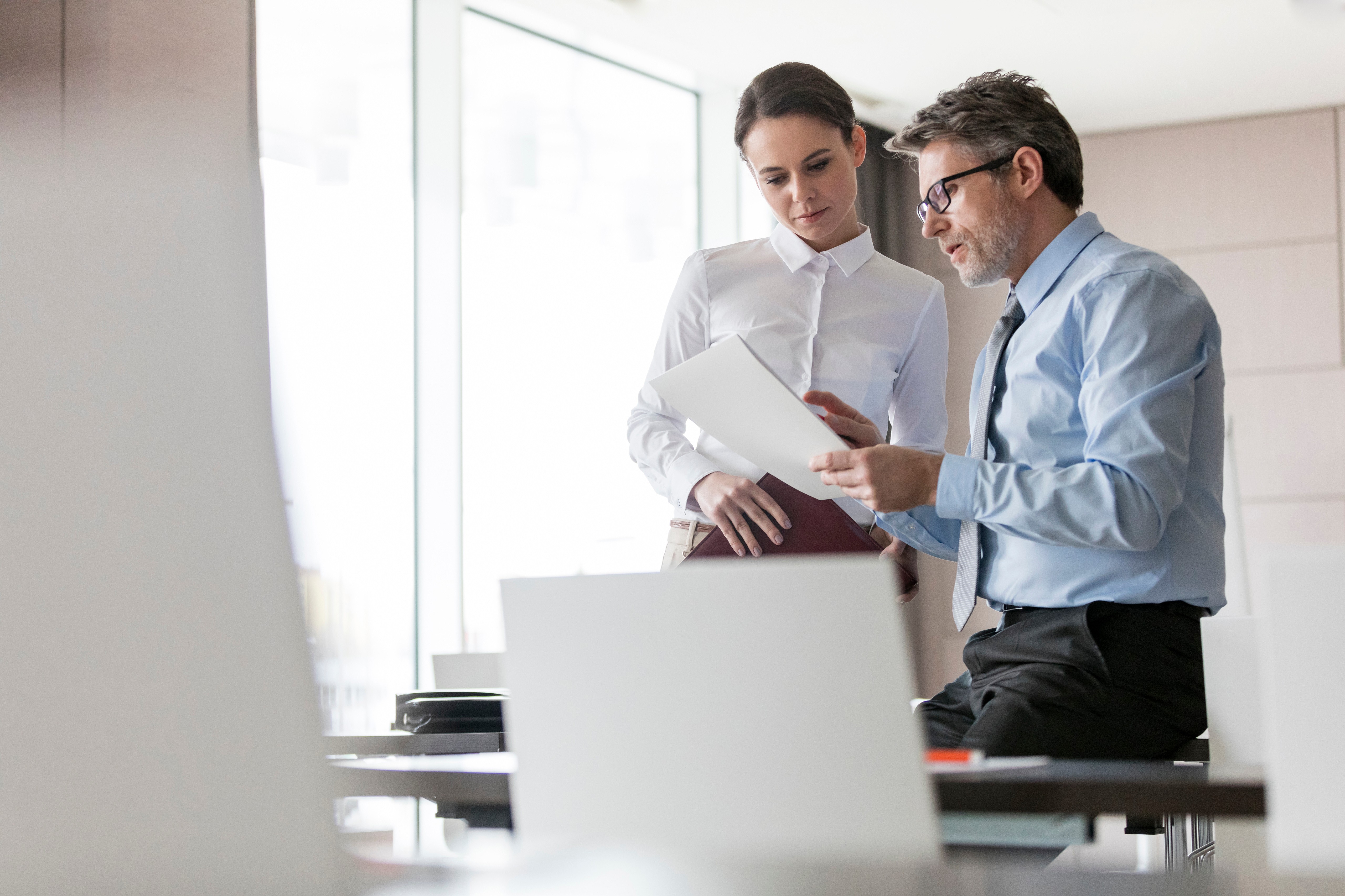 Two professionals reviewing a document together in a modern office, representing audit, assurance, and structured evaluation of organisational practices.
