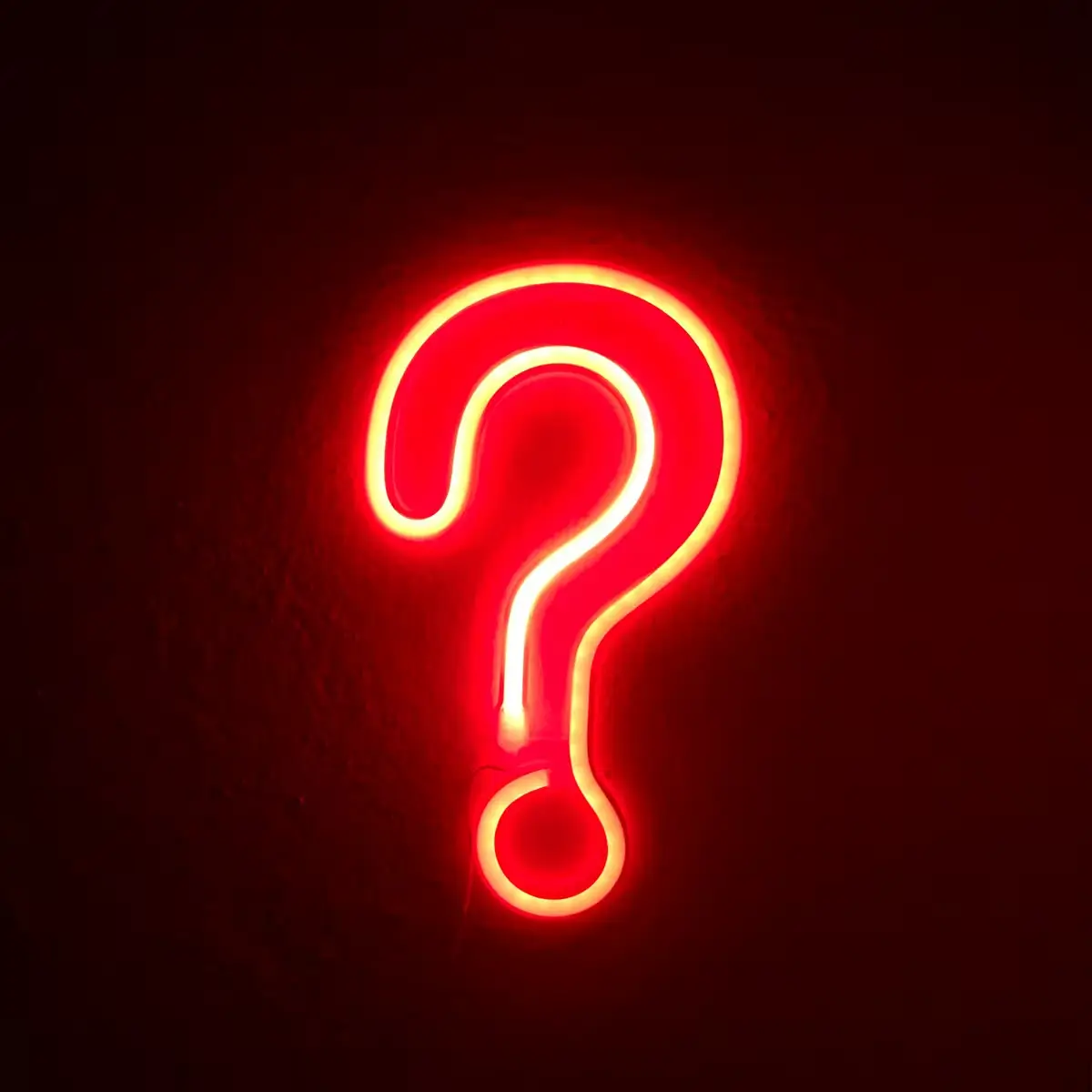 Neon red question mark glowing against a dark background, representing unanswered questions and the search for deeper insight.