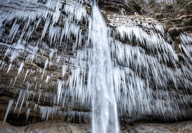  The frozen Peričnik Waterfall in Triglav National Park, Slovenia, during winter, featuring a massive wall of dramatic ice stalactites and long icicles surrounding the plunging water.
