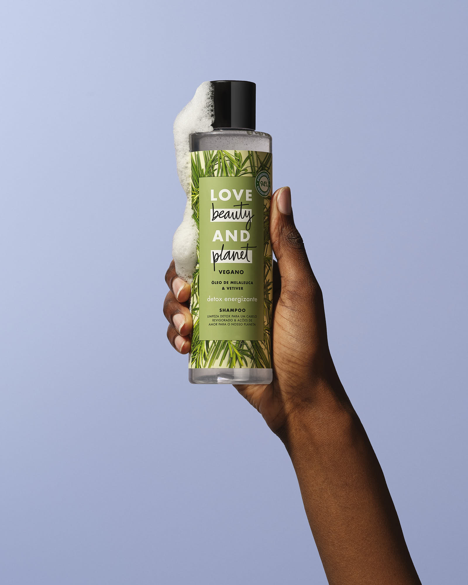 A hand holds a green bottle with a black cap, set against a light blue background.