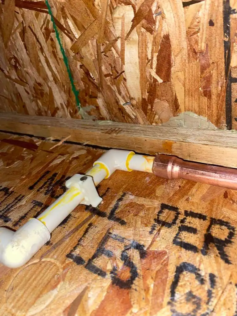 A secure transition joint connecting new plastic and copper plumbing pipes against a wooden joist during a residential pipe repair.