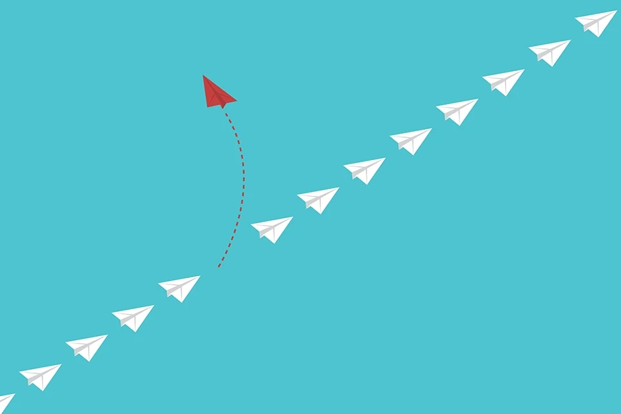 Illustration of a red paper airplane diverging from a path of white airplanes on a blue background.