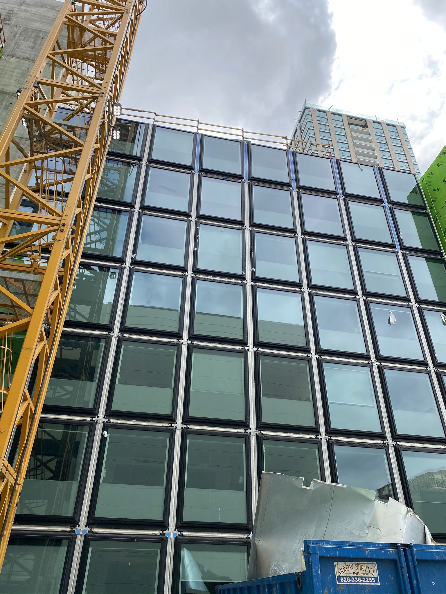 Seven levels of stacked modular guestrooms with a tower crane positioned on the left, readying the structure for exterior cladding installation.