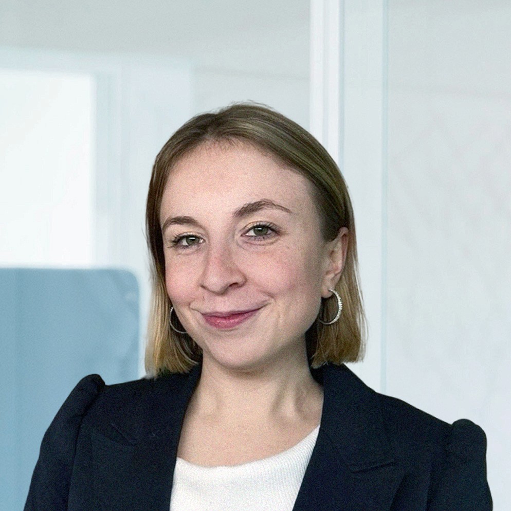 Woman playing paddle tennis, concentrating on her swing. A man watches from the sidelines.