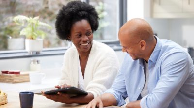 Caregiver and man sitting together, smiling while looking at a tablet in a home environment.