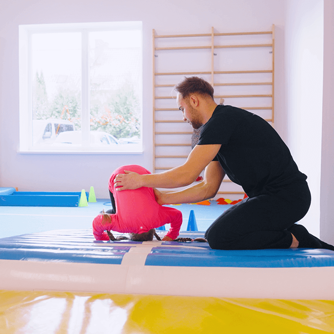 Trener Ernest asekurujący dziewczynkę do przewrotu w tył na sali akrobatycznej