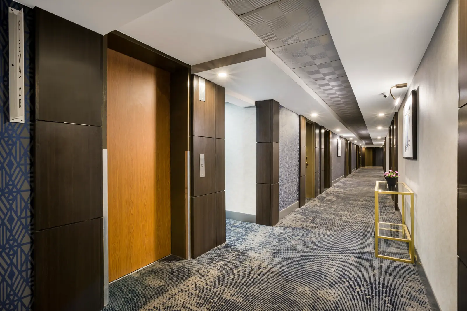 A modern hotel hallway with an elevator door and patterned carpet.
