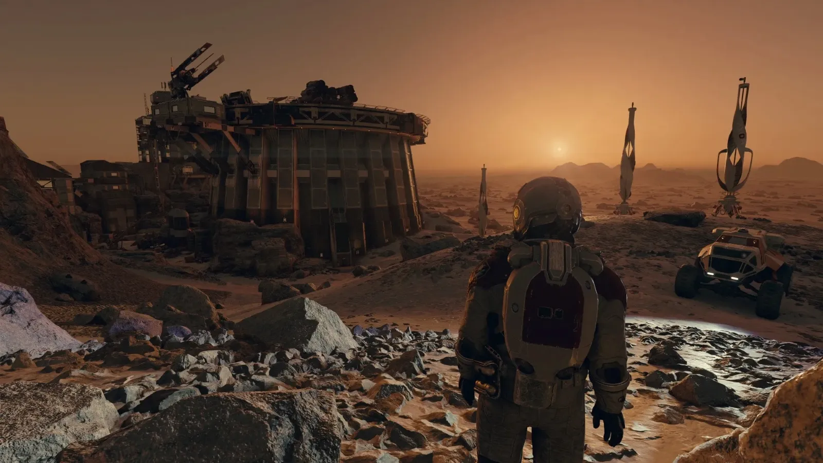 An astronaut in a spacesuit stands on a rocky Mars-like landscape at sunset, gazing towards a futuristic colony structure with antenna towers and a rover, emphasizing themes of space exploration and colonization.