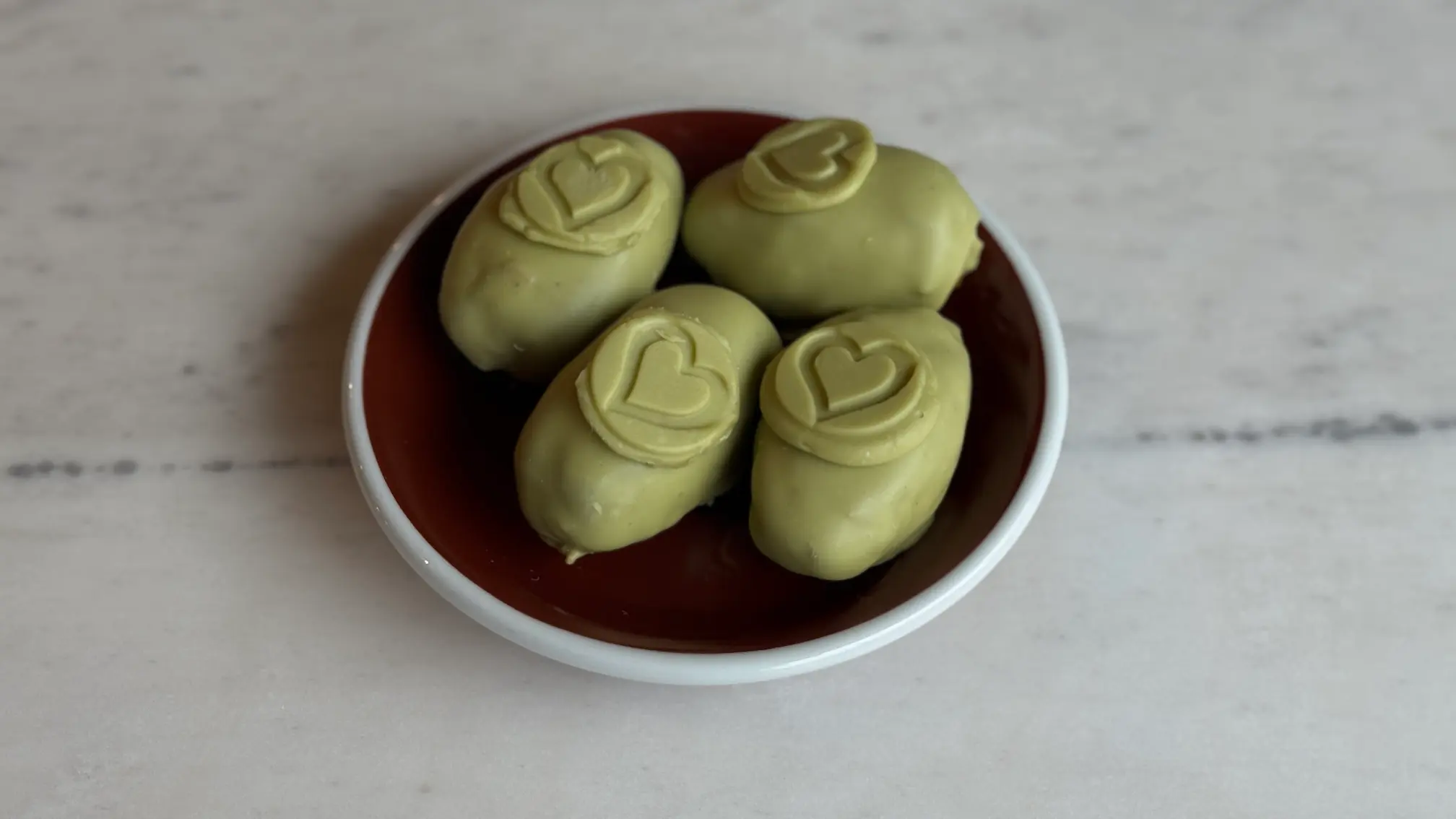 Here are alt text descriptions in English for these three images:  "Four heart-shaped pistachio mousse cakes with swirl pattern on white plate