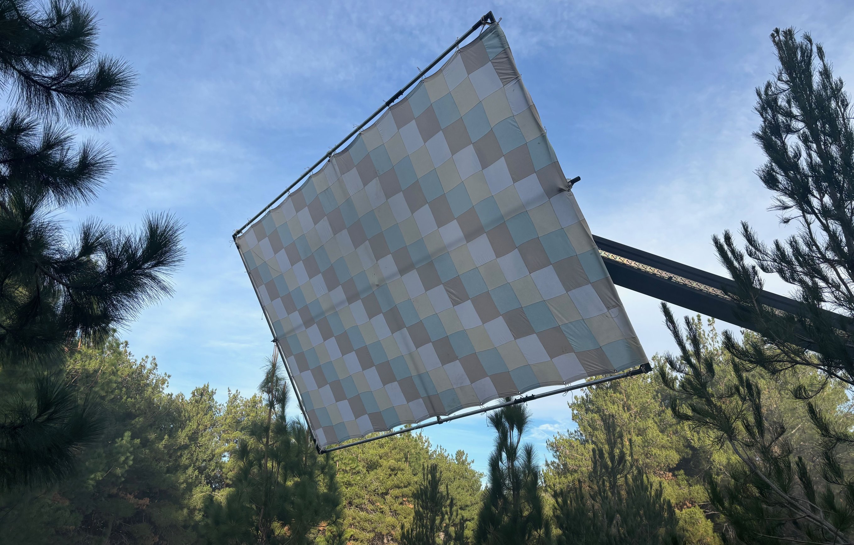 12x20 checker bounce tilted at an angle with the full checker face visible, framed through pine branches against blue sky and light cloud.