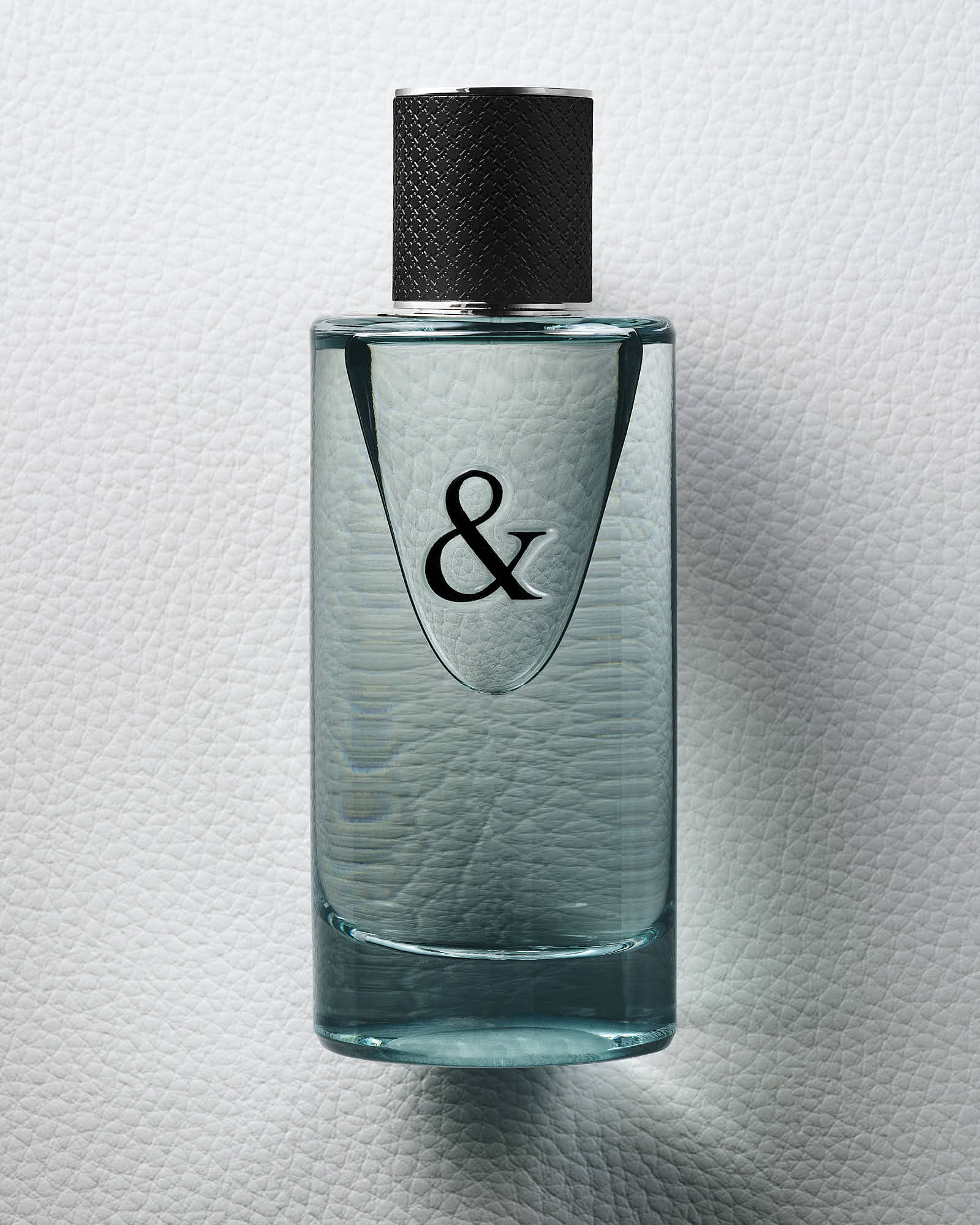 A teal glass perfume bottle with a black cap and an ampersand symbol on the front, against a white background.
