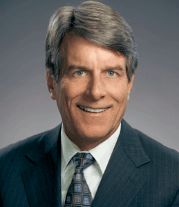 Professional-looking man with gray hair wearing a suit, smiling against a neutral background.