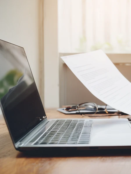 Laptop sitting on desk with resumes