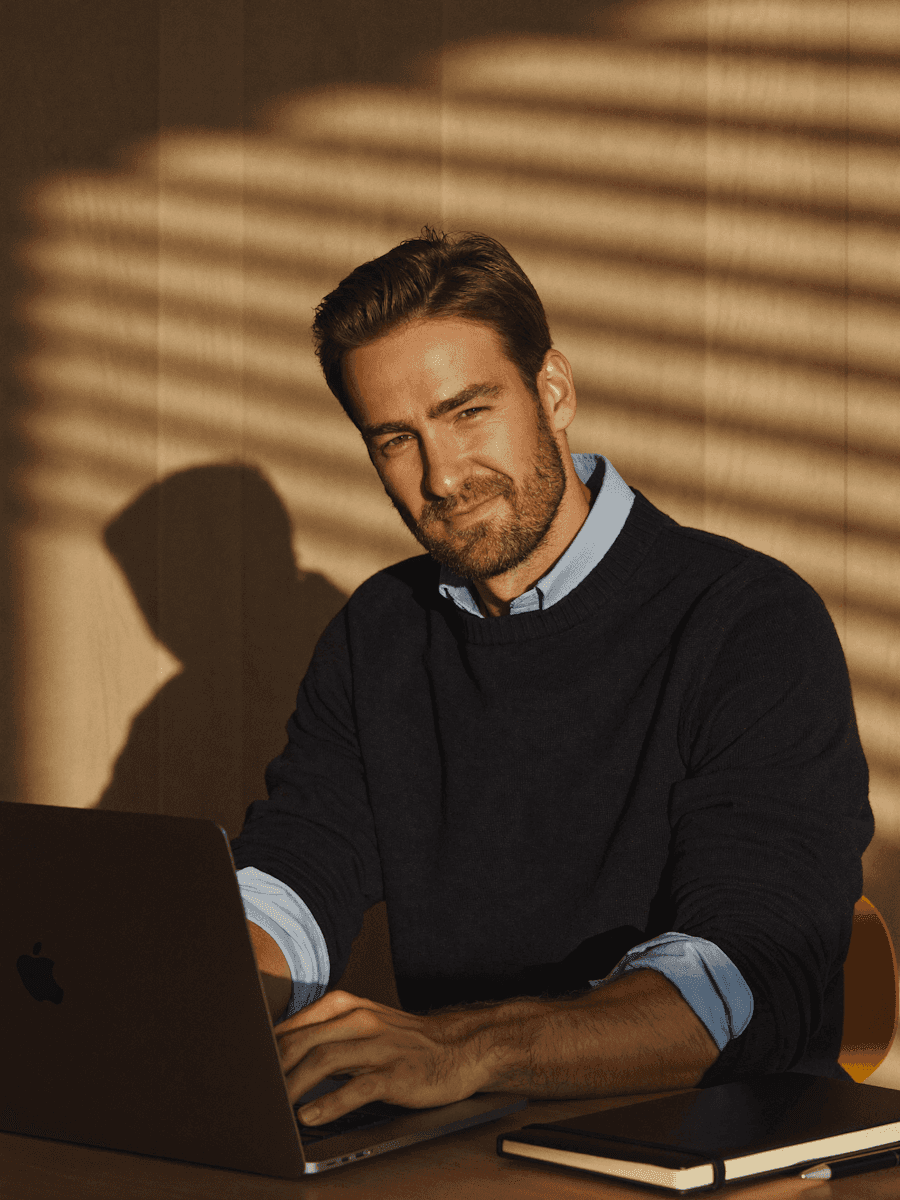 Man working on a laptop in warm dramatic light with shadow stripes on the wall behind him