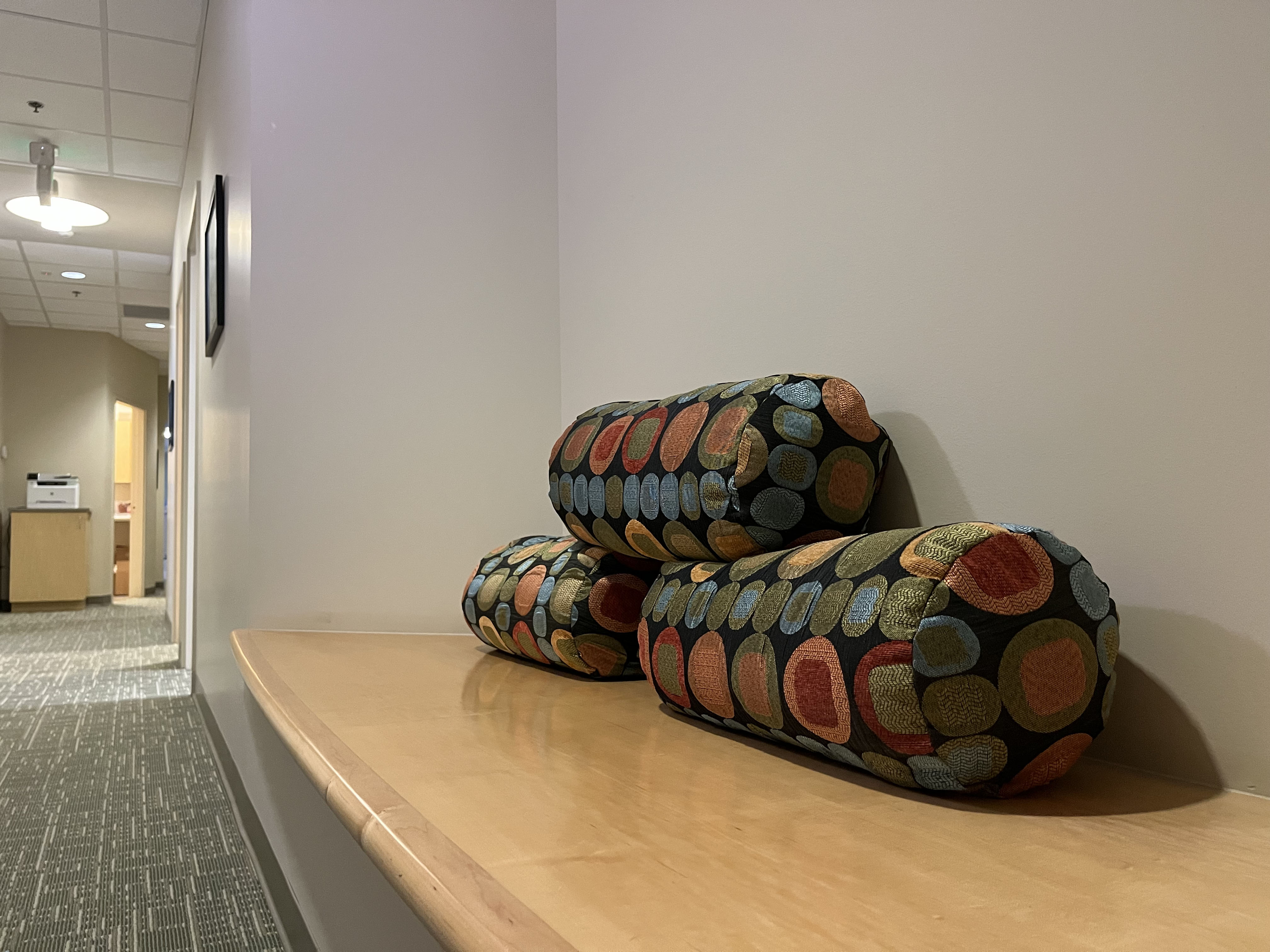 Three stacked, camouflaged military-style backpacks rest on a wooden surface in a corridor with soft lighting.