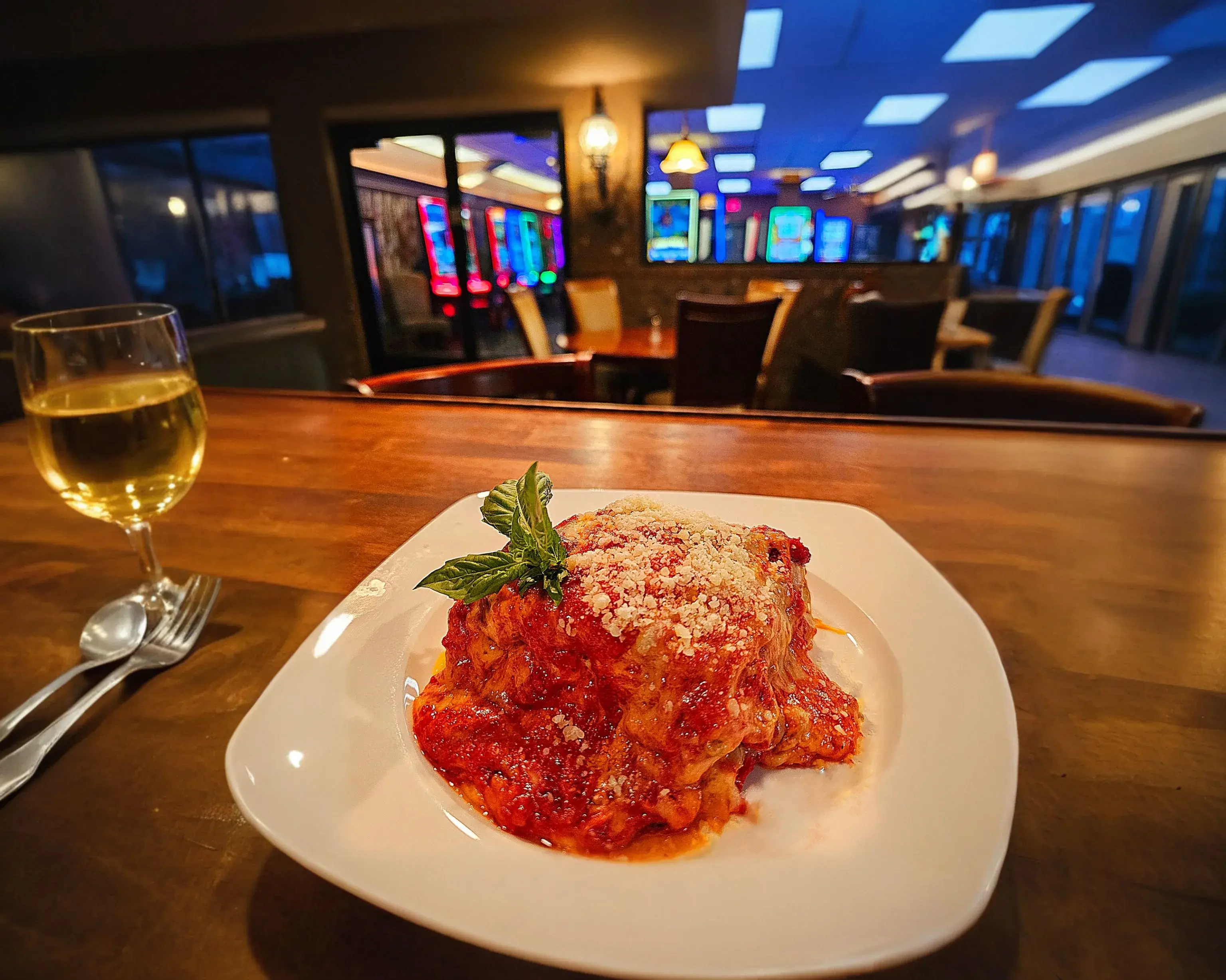 A rich and cheesy lasagna paired with a glass of red wine, served on a rustic wooden table at Dueling Pistols Restaurant.