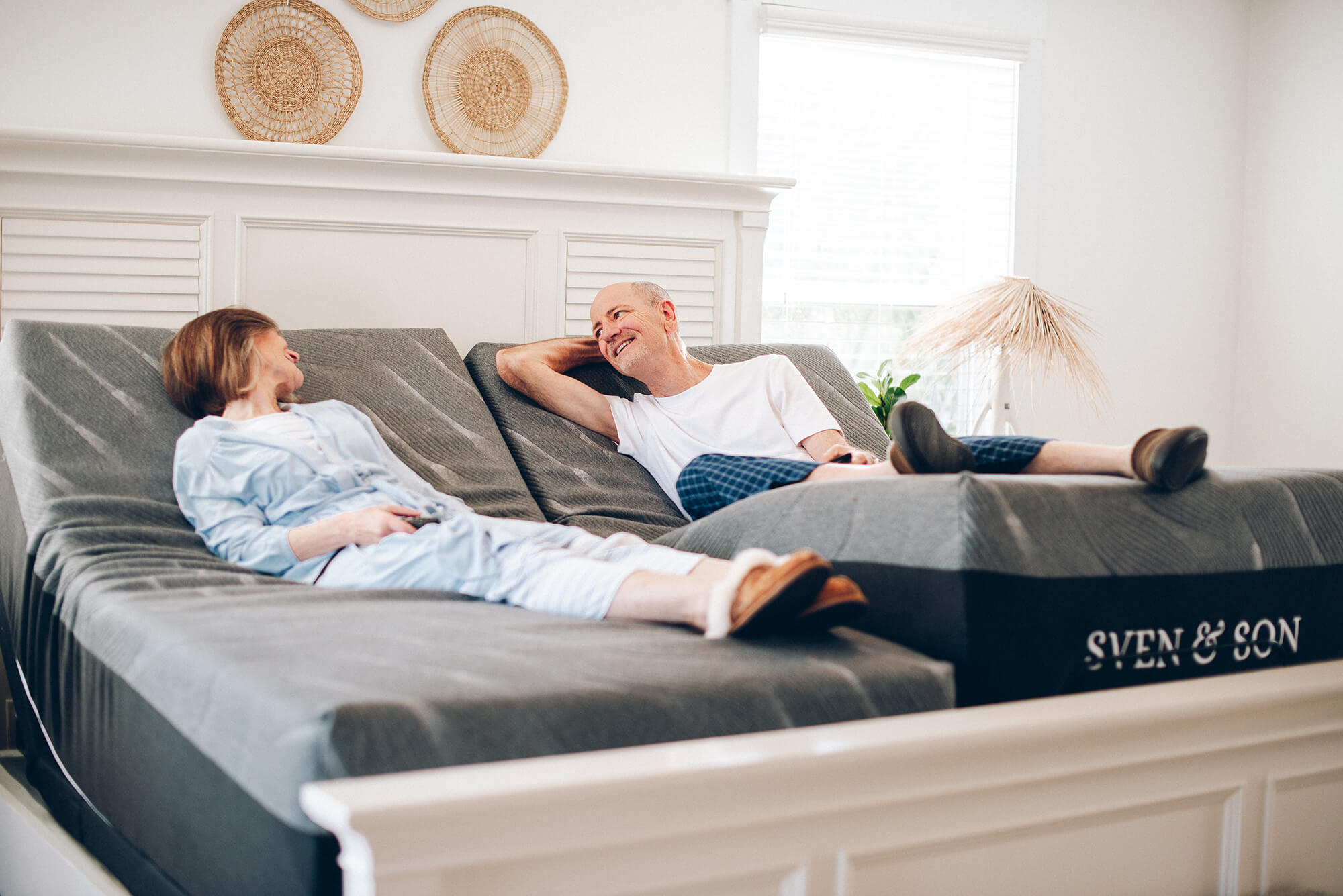 A couple are lying on a dual adjustable bed with different settings, showing how the bed can accommodate different preferences for back and leg elevations.